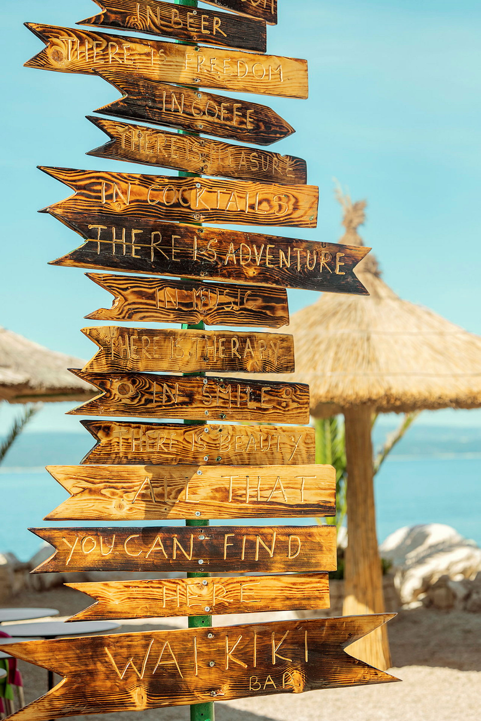 Træpile med indgraveret tekst, der fungerer som skilte ved en strandbar. (AI-genereret tekst)