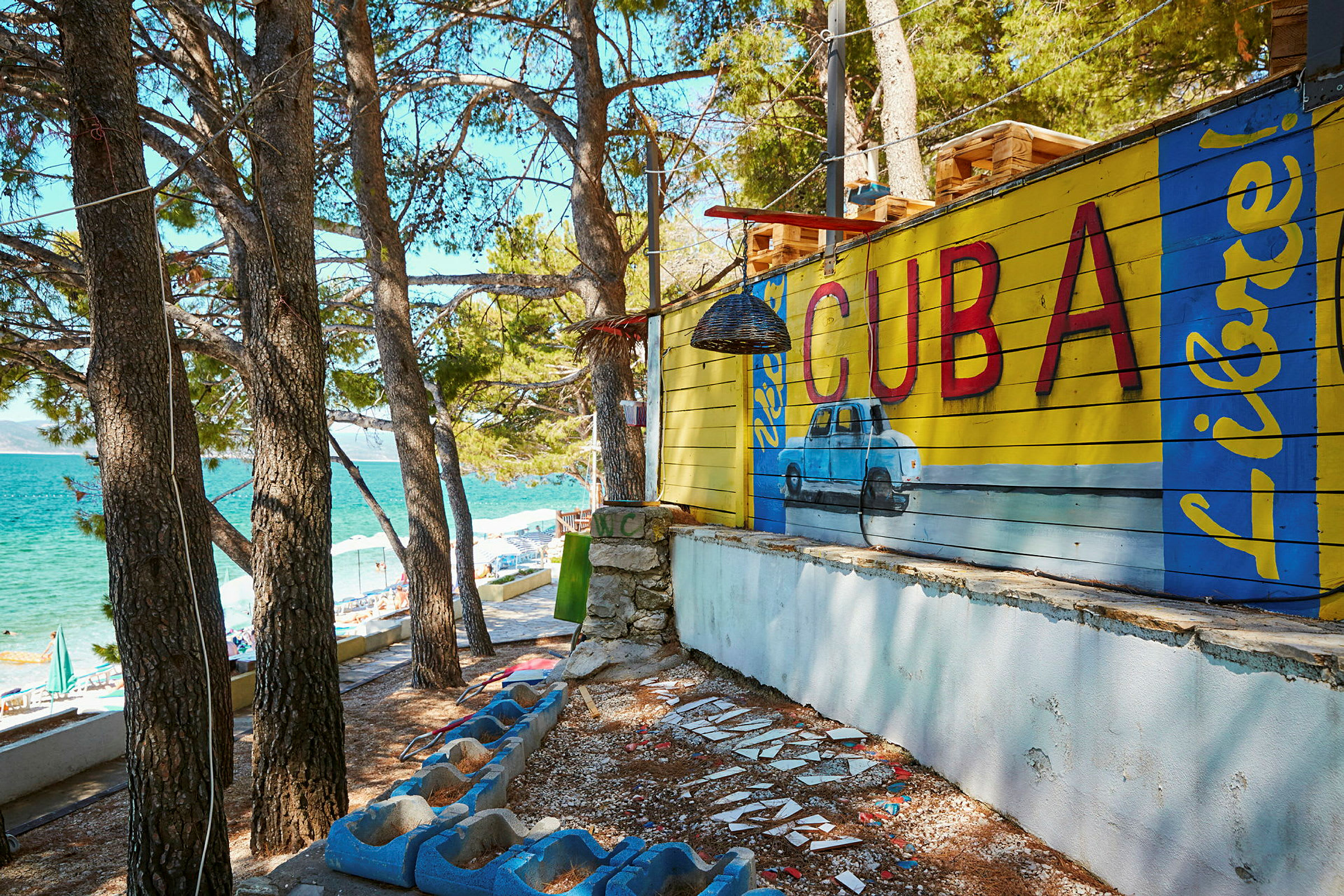 Vægmaling med teksten 'Cuba' og en blå bil i tropisk miljø. (AI-genereret tekst)