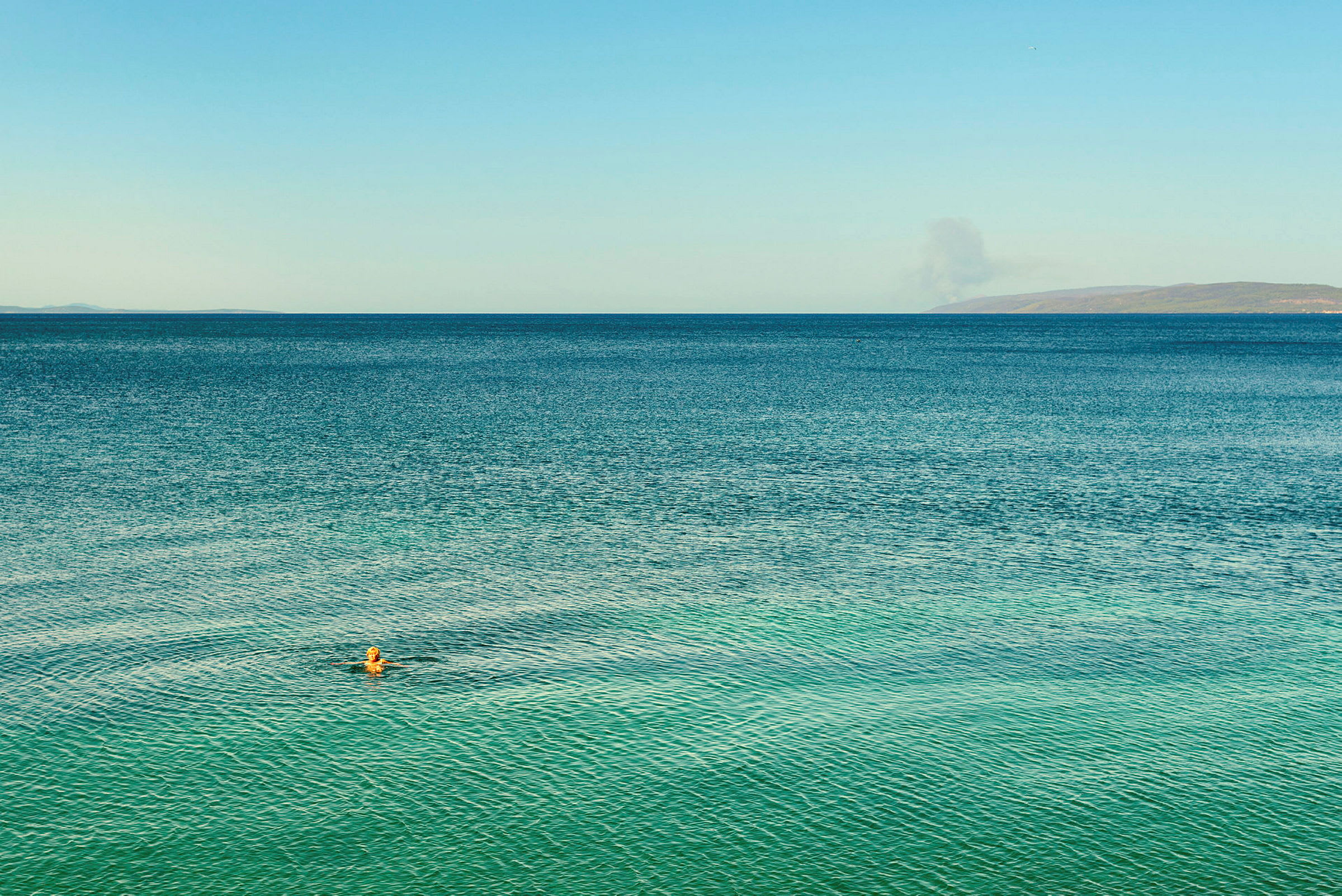 Person svømmer i havet under en blå himmel. (AI-genereret tekst)