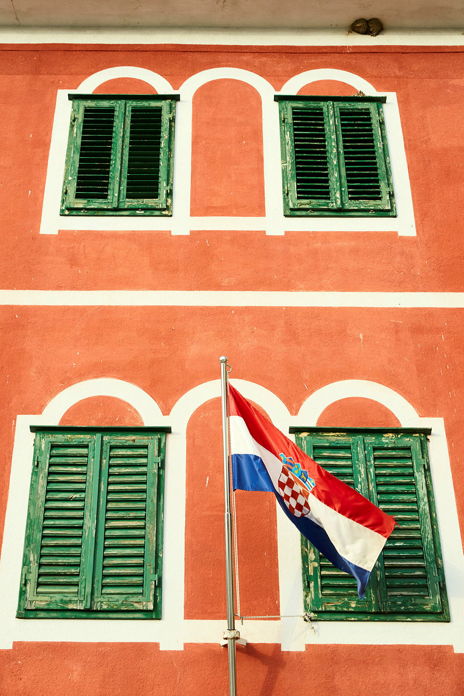 En rød bygning med grønne skodder og Kroatiens flag foran. (AI-genereret tekst)