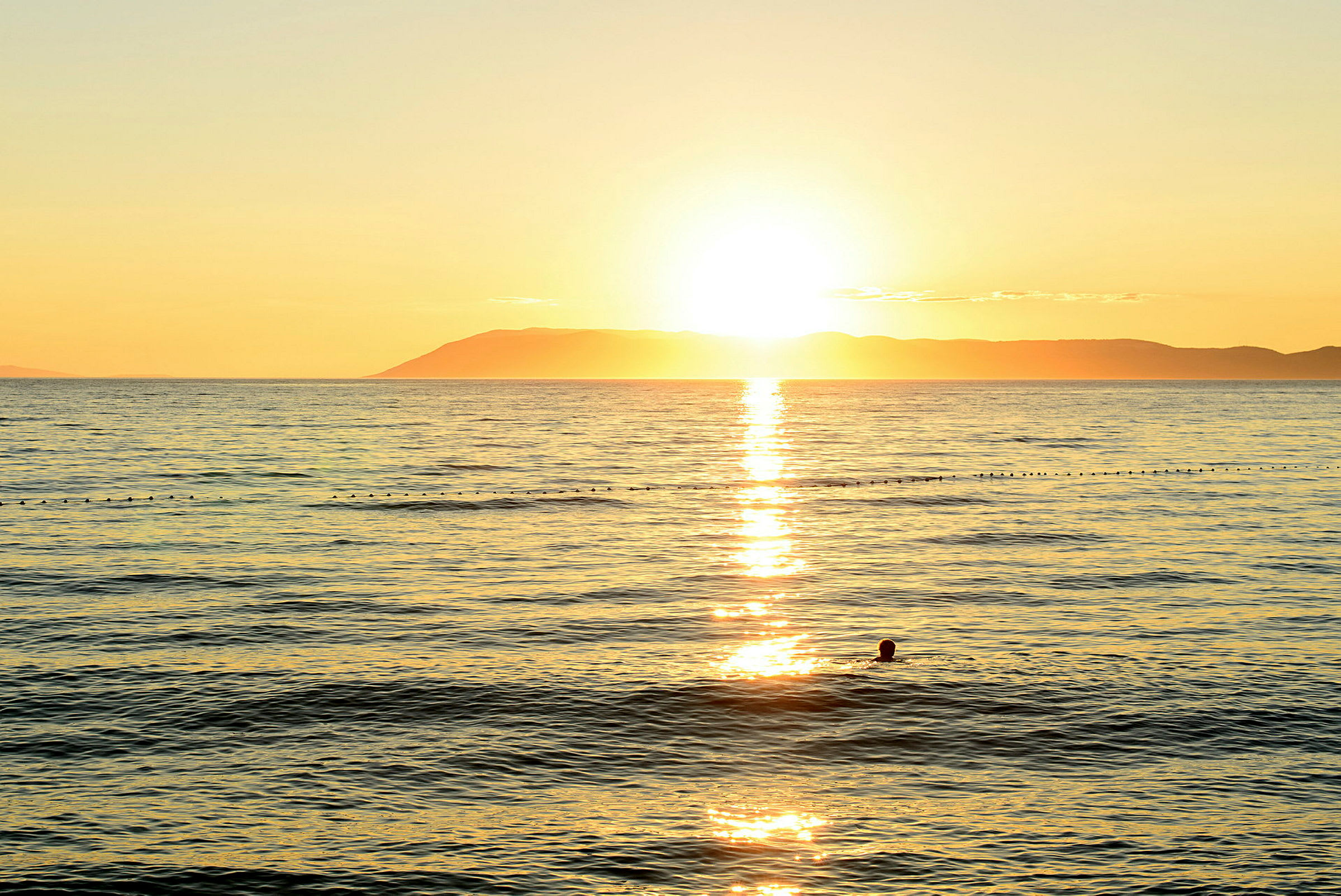 Solnedgang over havet med en silhuet af en svømmende person. (AI-genereret tekst)