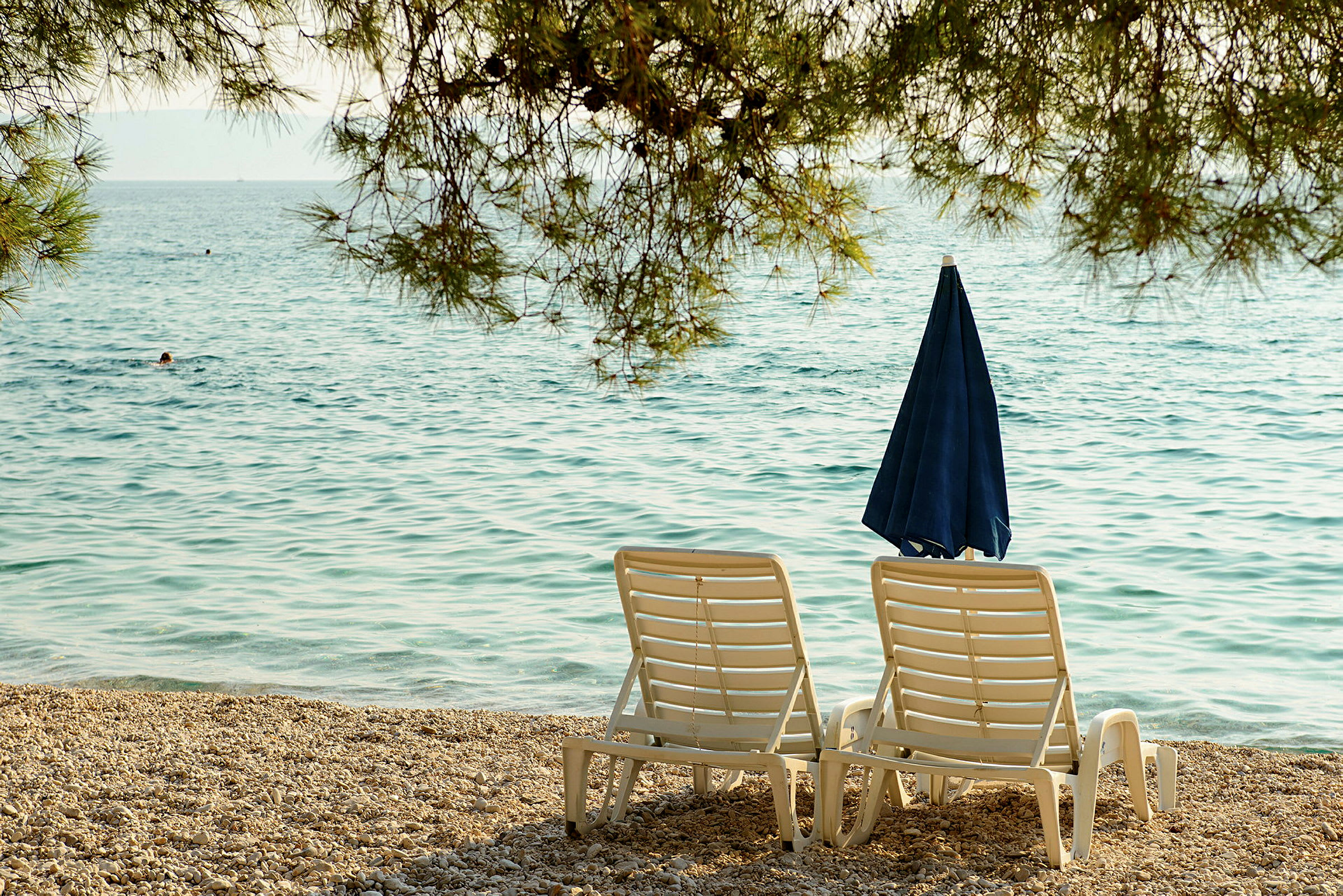 To liggestole og en parasol ved en stenstrand med havet i baggrunden. (AI-genereret tekst)