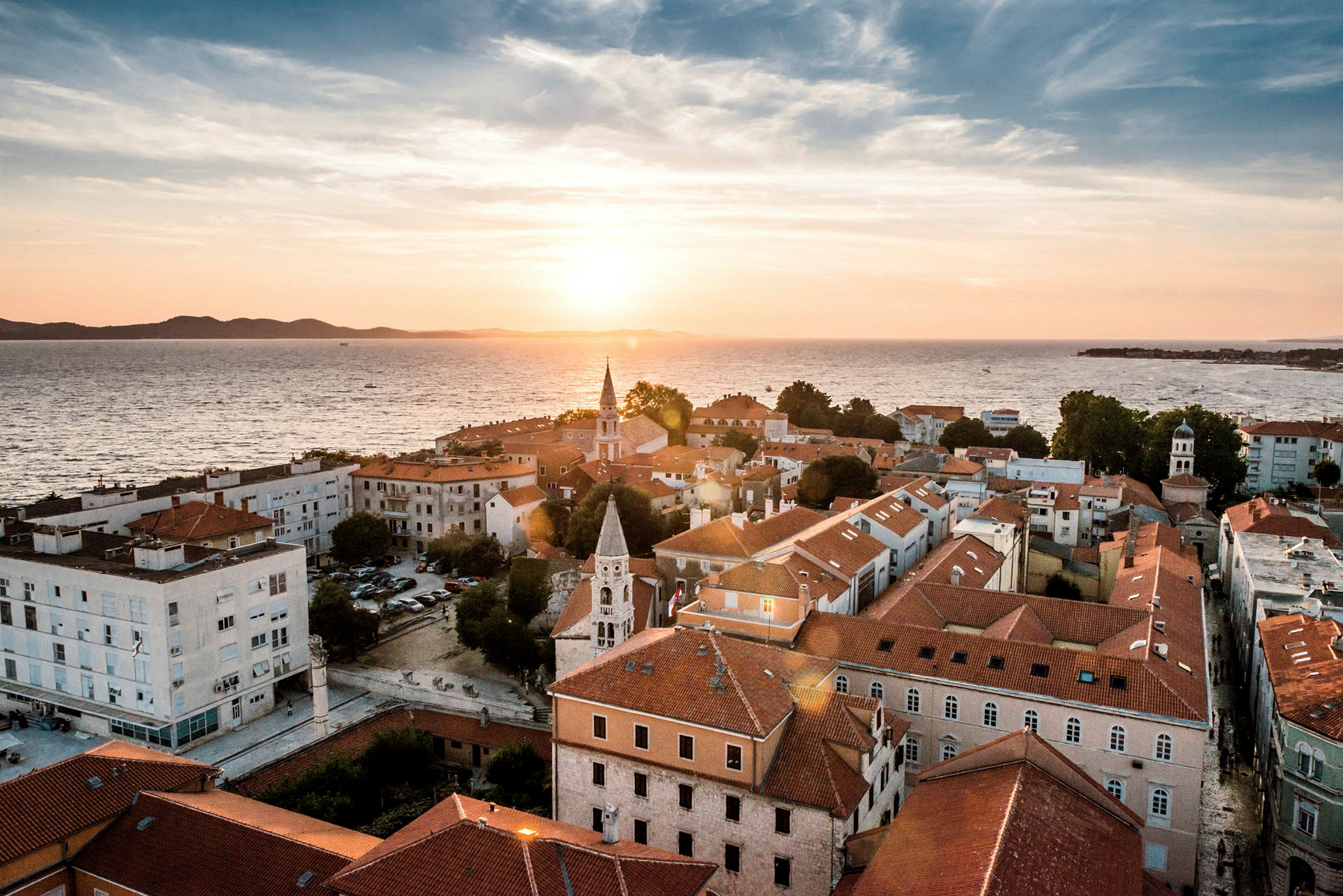 Udsigt over en kystby med røde tegltage ved solnedgang. (AI-genereret tekst)