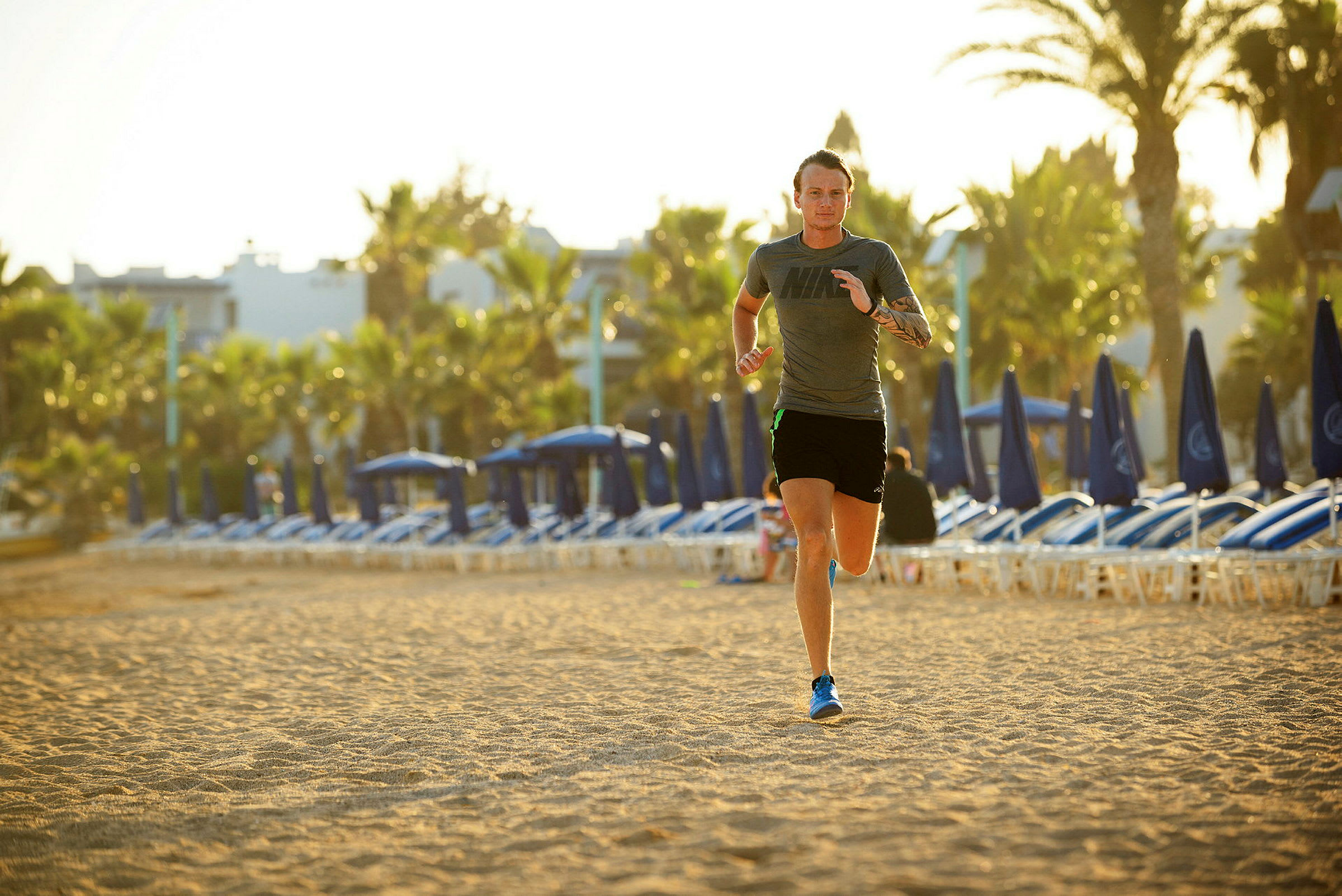 Person løber på en solrig strand med palmer og liggestole i baggrunden. (AI-genereret tekst)