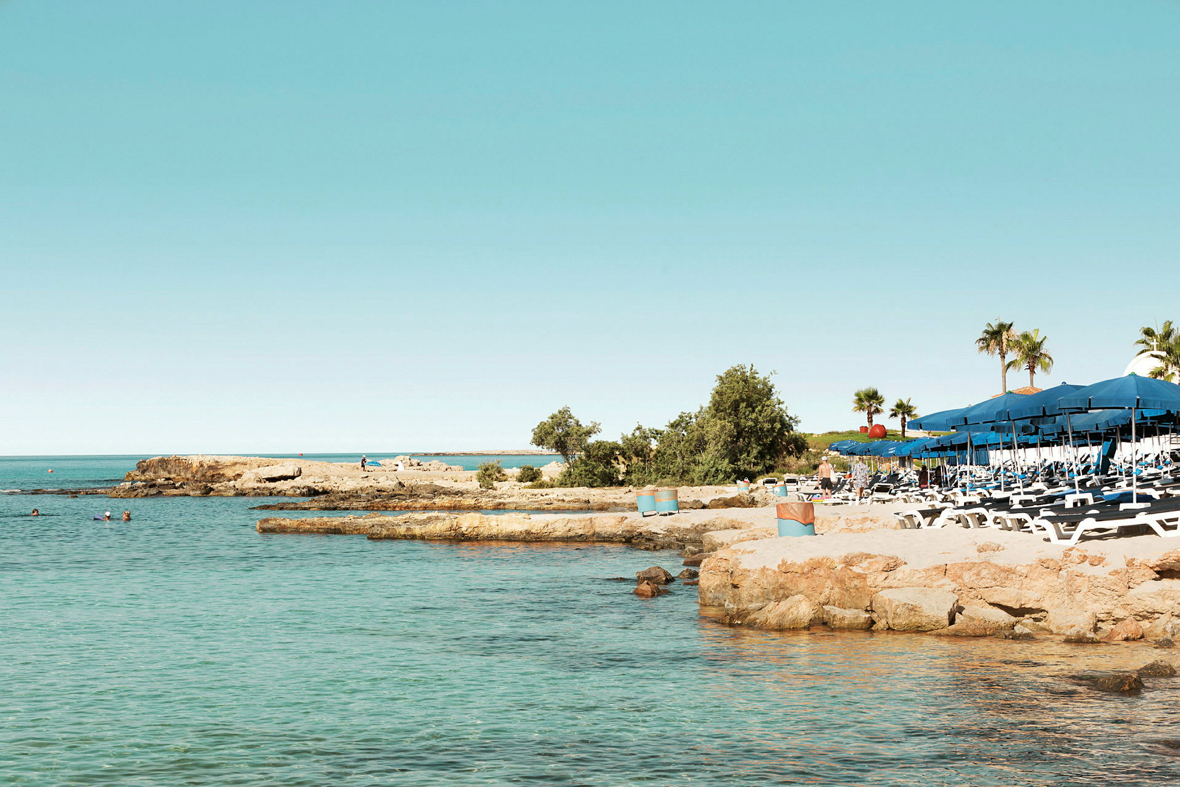 Billede af en strand med liggestole og parasoller ved siden af klart vand. (AI-genereret tekst)