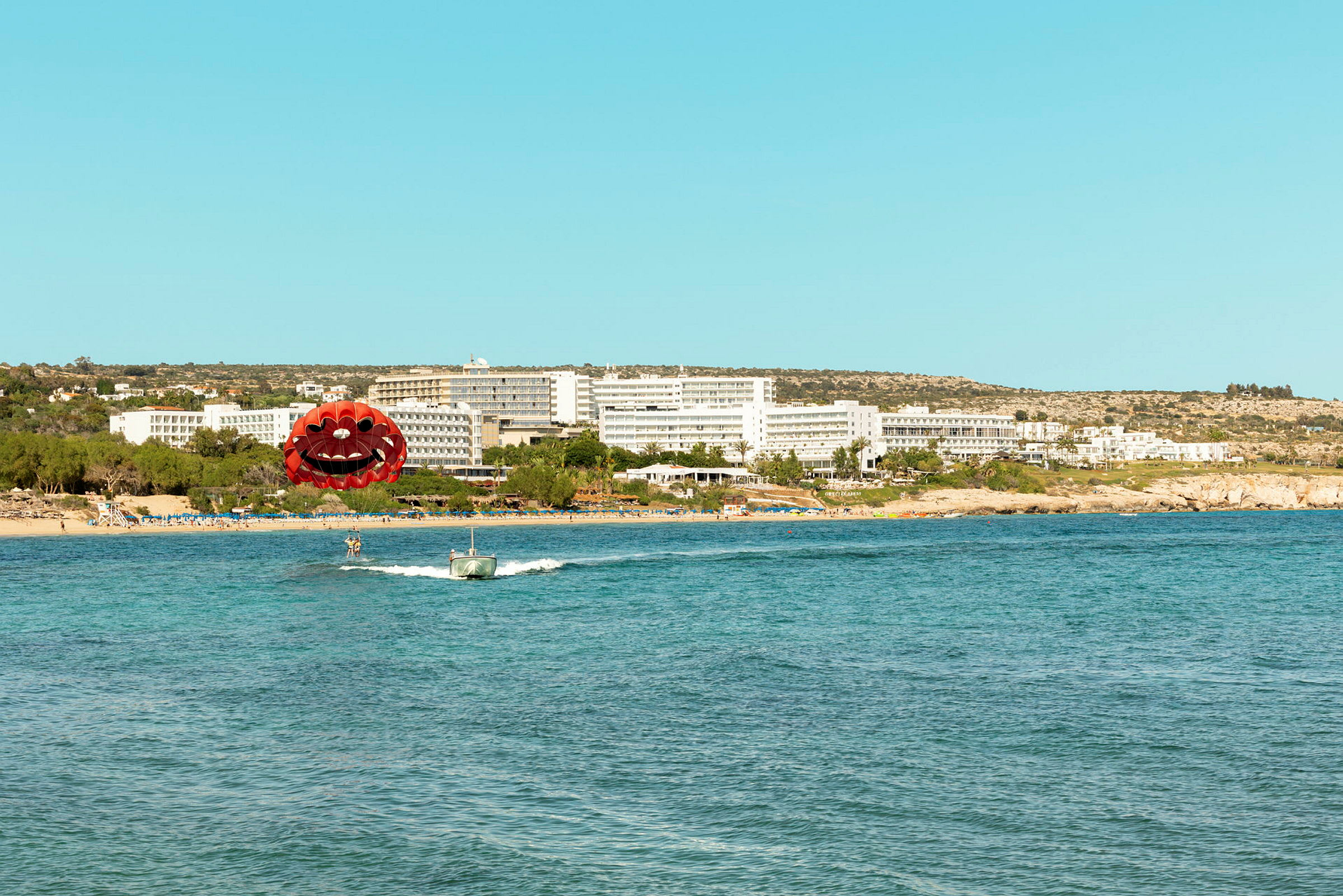 Billede af en strand med et hotel i baggrunden og en person, der parasailer foran. (AI-genereret tekst)