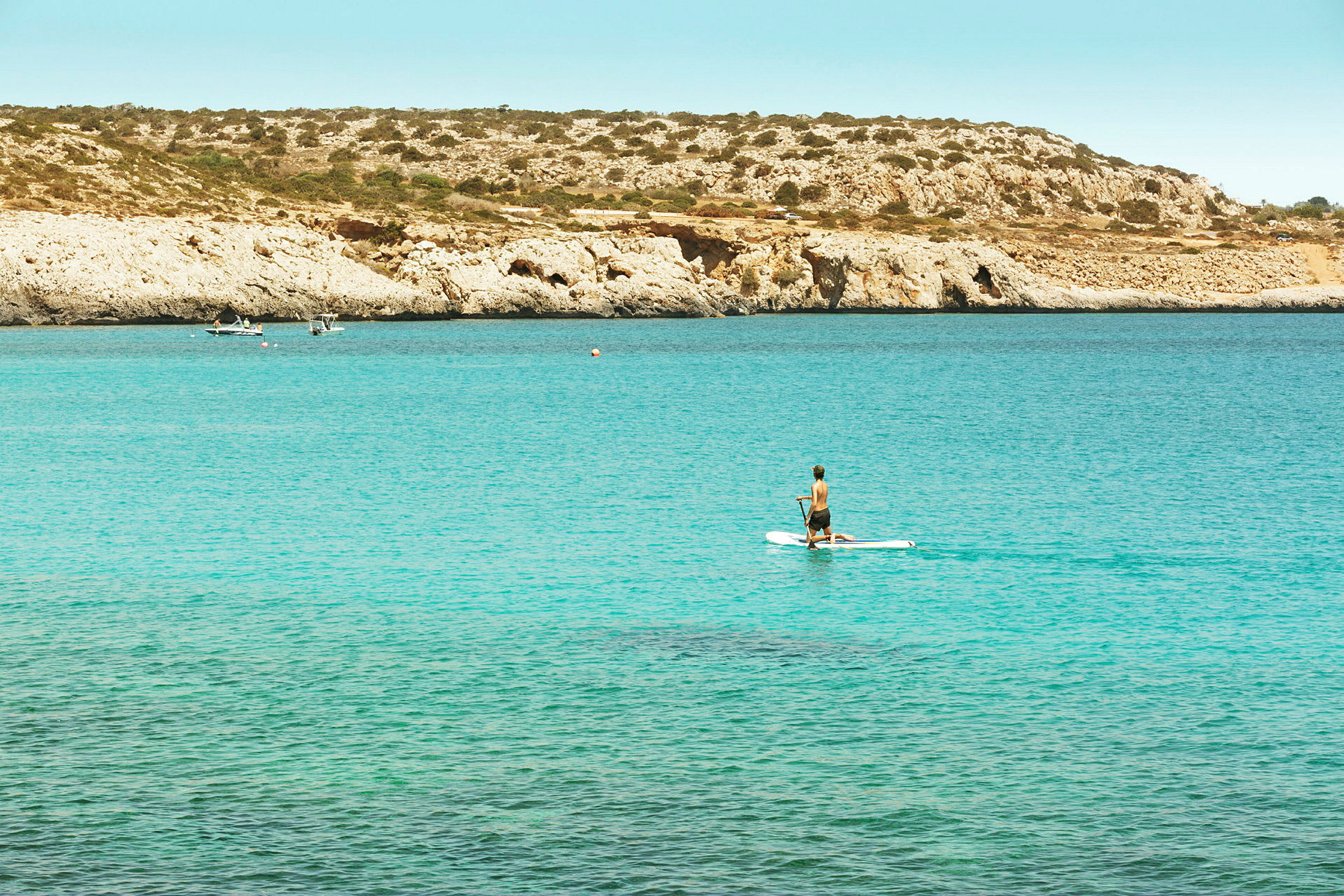 En person, der padler på et paddleboard med klipper og hav i baggrunden. (AI-genereret tekst)
