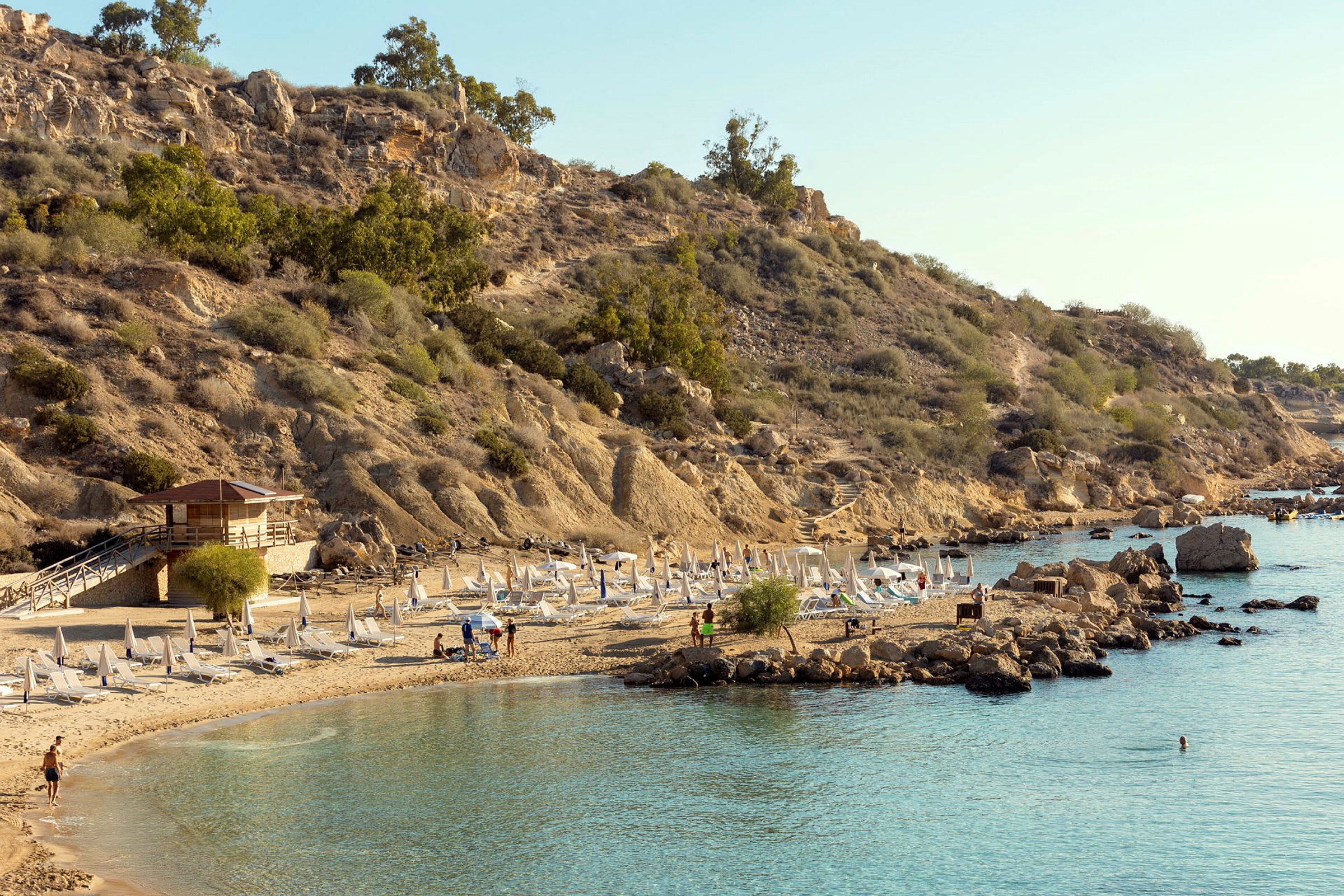 En klippekyst med liggestole og parasoller på en sandstrand. (AI-genereret tekst)