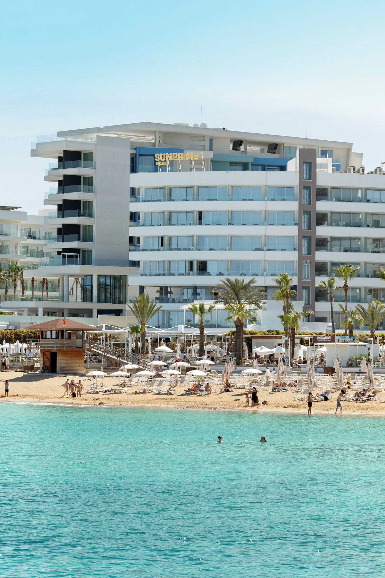 Et strandhotel med liggestole og turkis hav i forgrunden. (AI-genereret tekst)