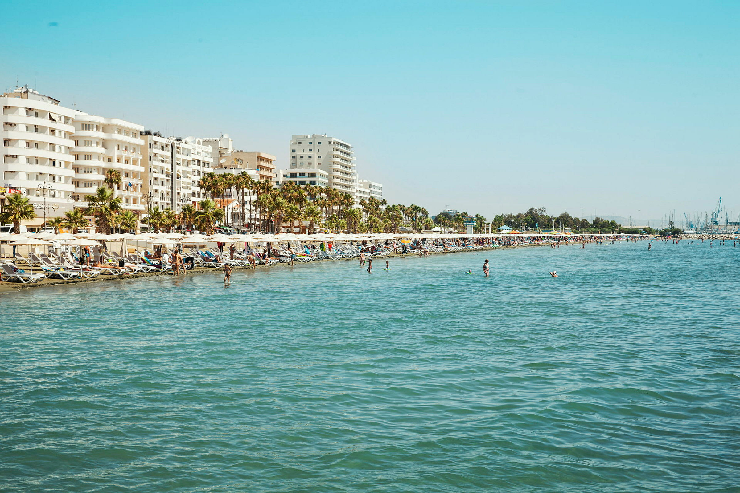 Strand med liggestole og parasoller, ved en by med bygninger i flere etager. (AI-genereret tekst)