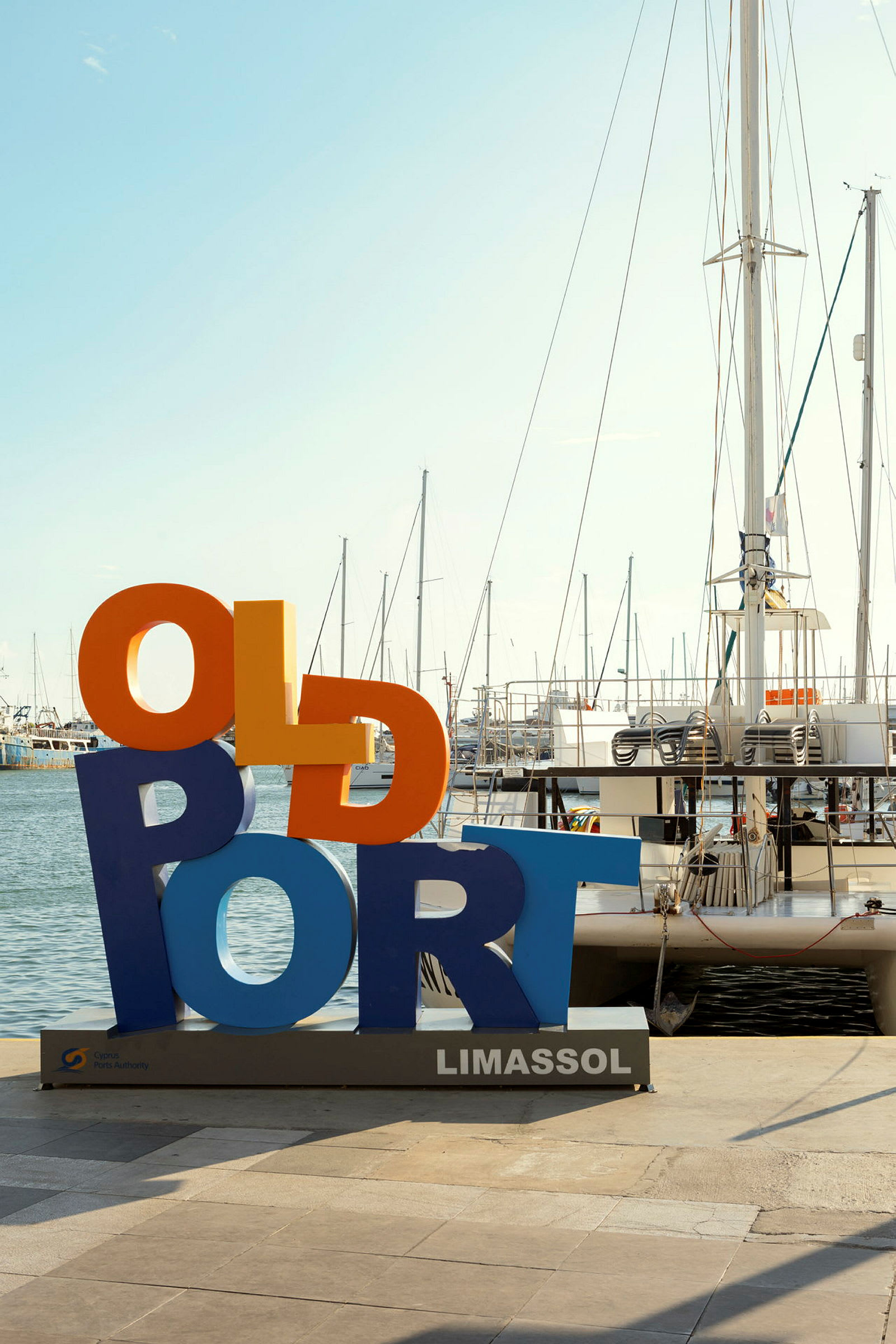 Farverigt skilt med teksten 'Old Port' ved havnen i Limassol, sejlbåde i baggrunden. (AI-genereret tekst)