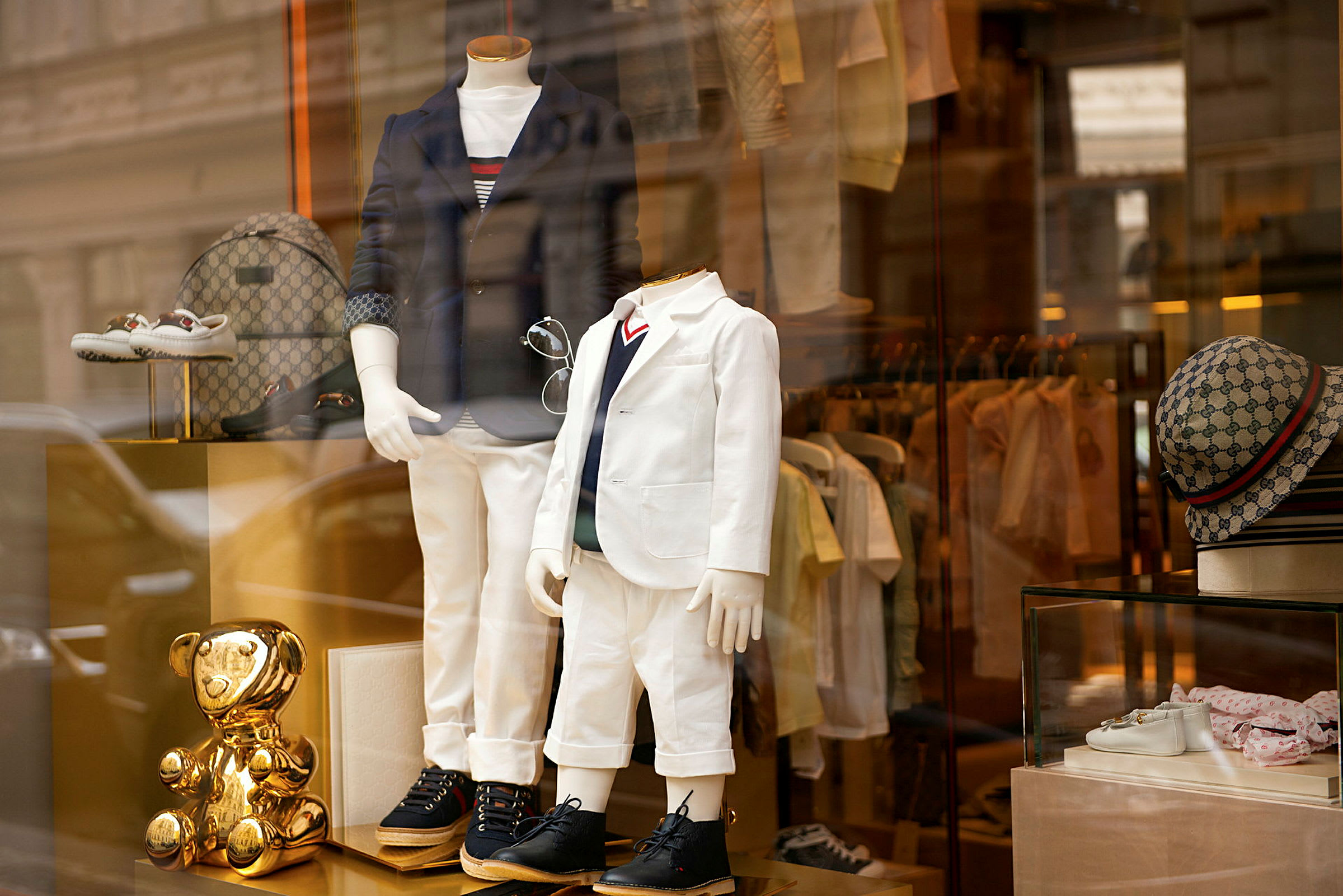 Butiksvindue med to mannequinfigurer klædt i elegante outfits, omgivet af tilbehør og en gylden pyntegenstand. (AI-genereret tekst)