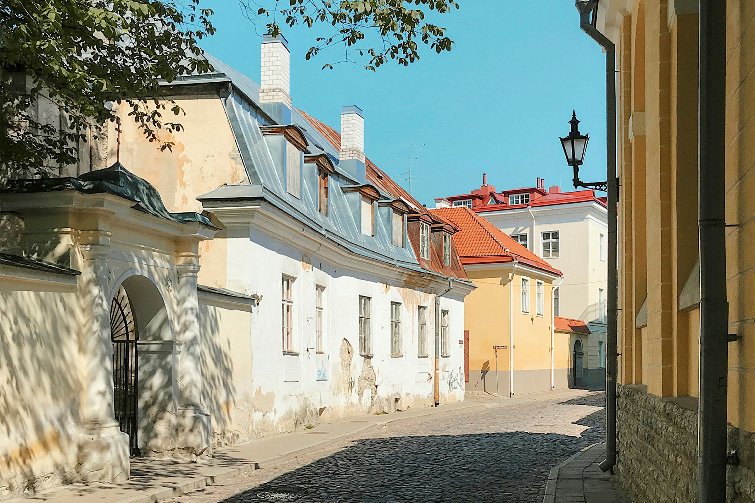 En smal gade omgivet af gamle bygninger med tegltage og bliktag under en klar blå himmel. (AI-genereret tekst)