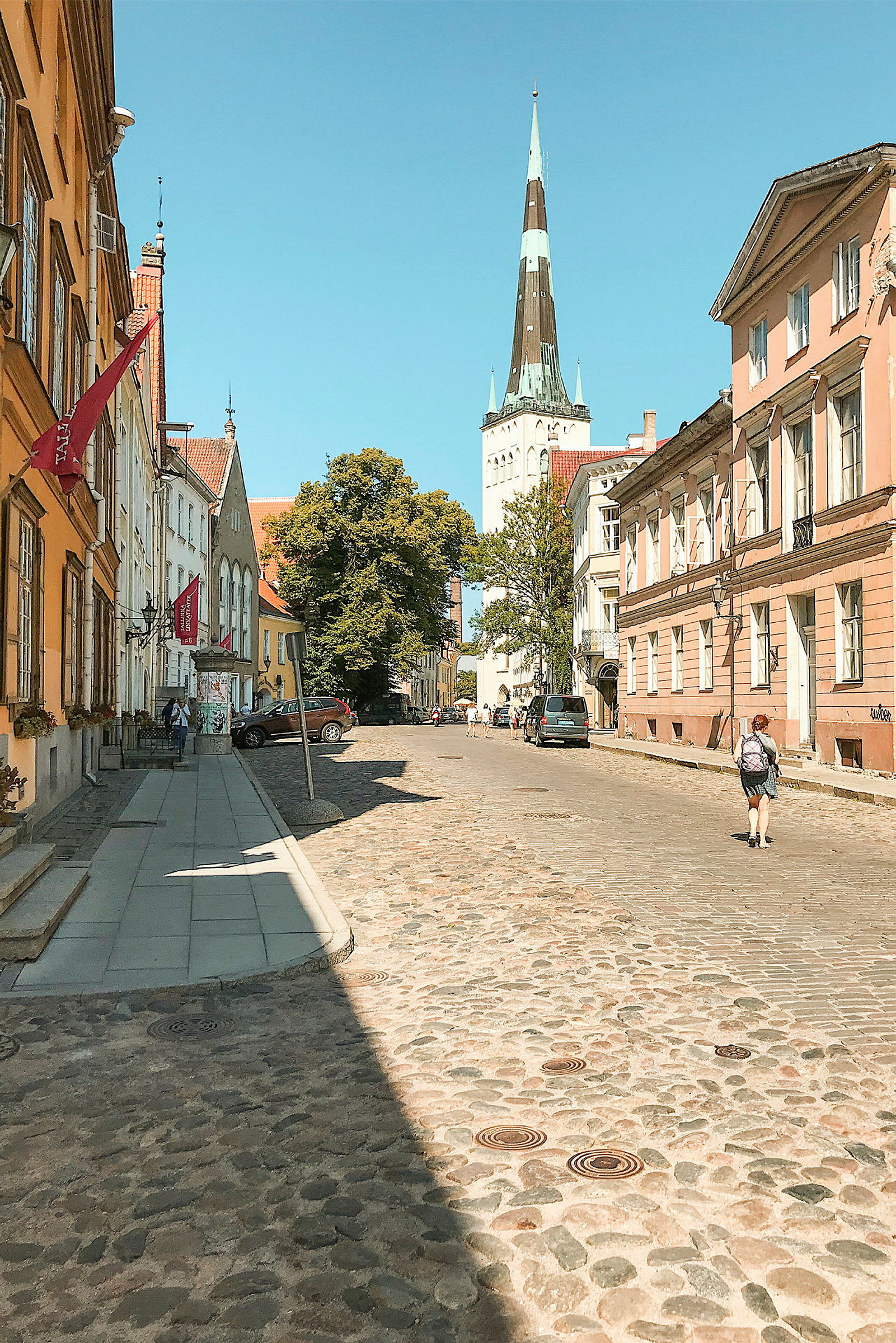En brostensbelagt gade omgivet af farverige ældre bygninger, med et kirkespir synligt i baggrunden under en klar blå himmel. (AI-genereret tekst)