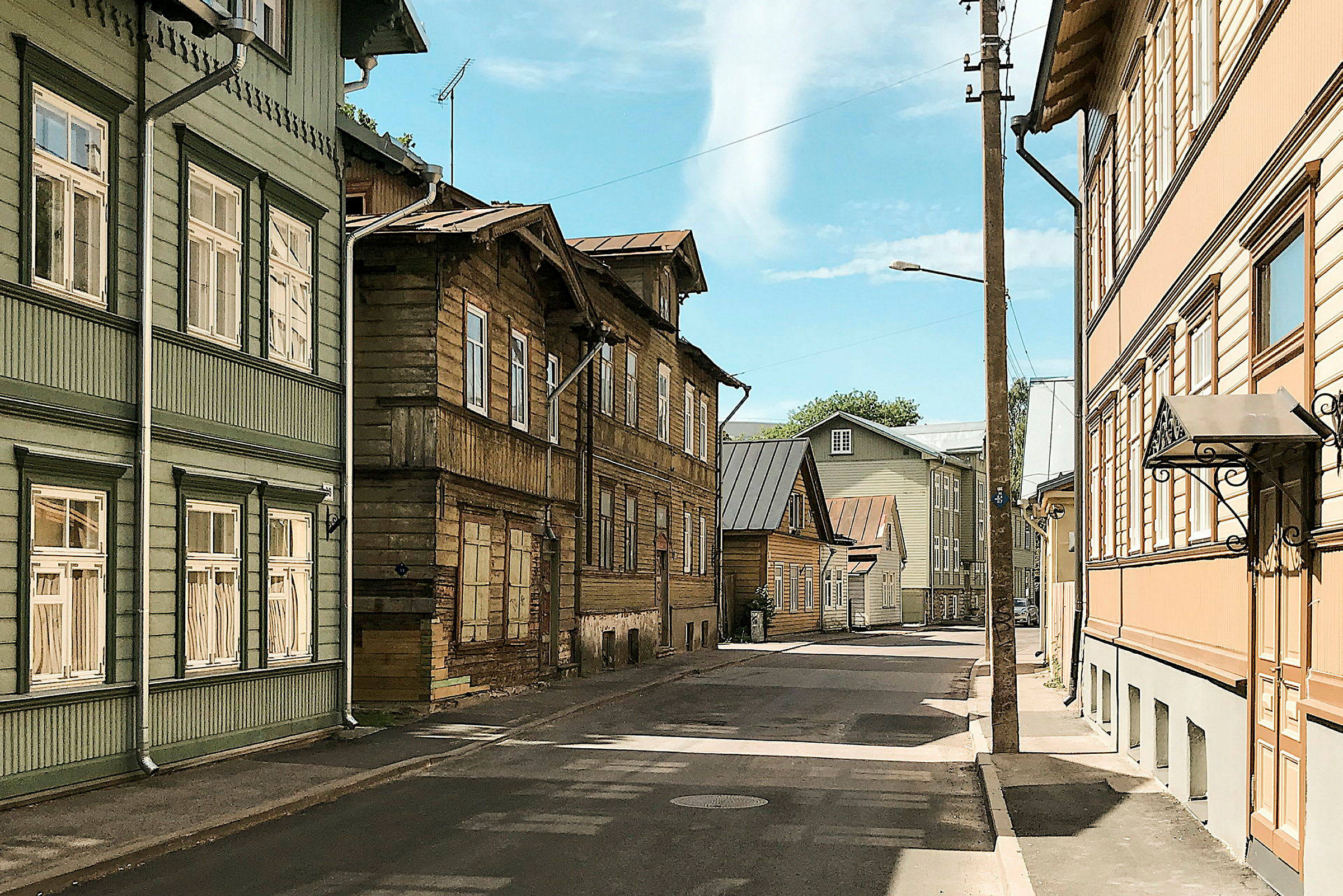 En gade omgivet af huse i træ med forskellige farver, blå himmel ses i baggrunden. (AI-genereret tekst)