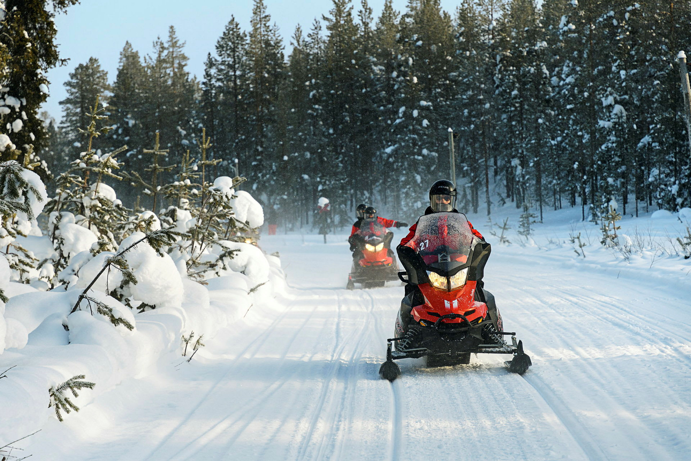 Snescootere kører på en sneklædt vej omgivet af skov. (AI-genereret tekst)