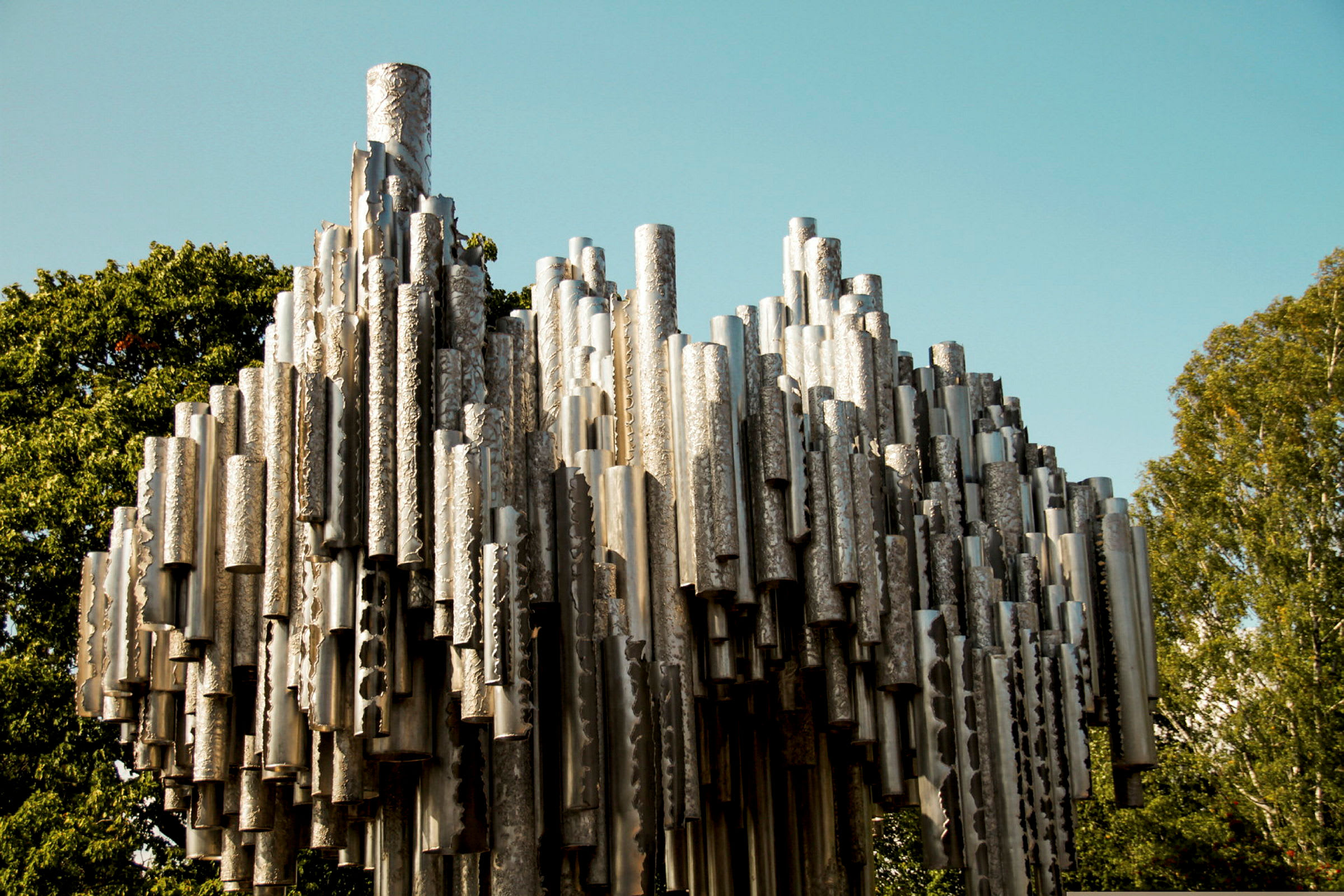 En metalskulptur omgivet af grønne træer med klar blå himmel i baggrunden. (AI-genereret tekst)