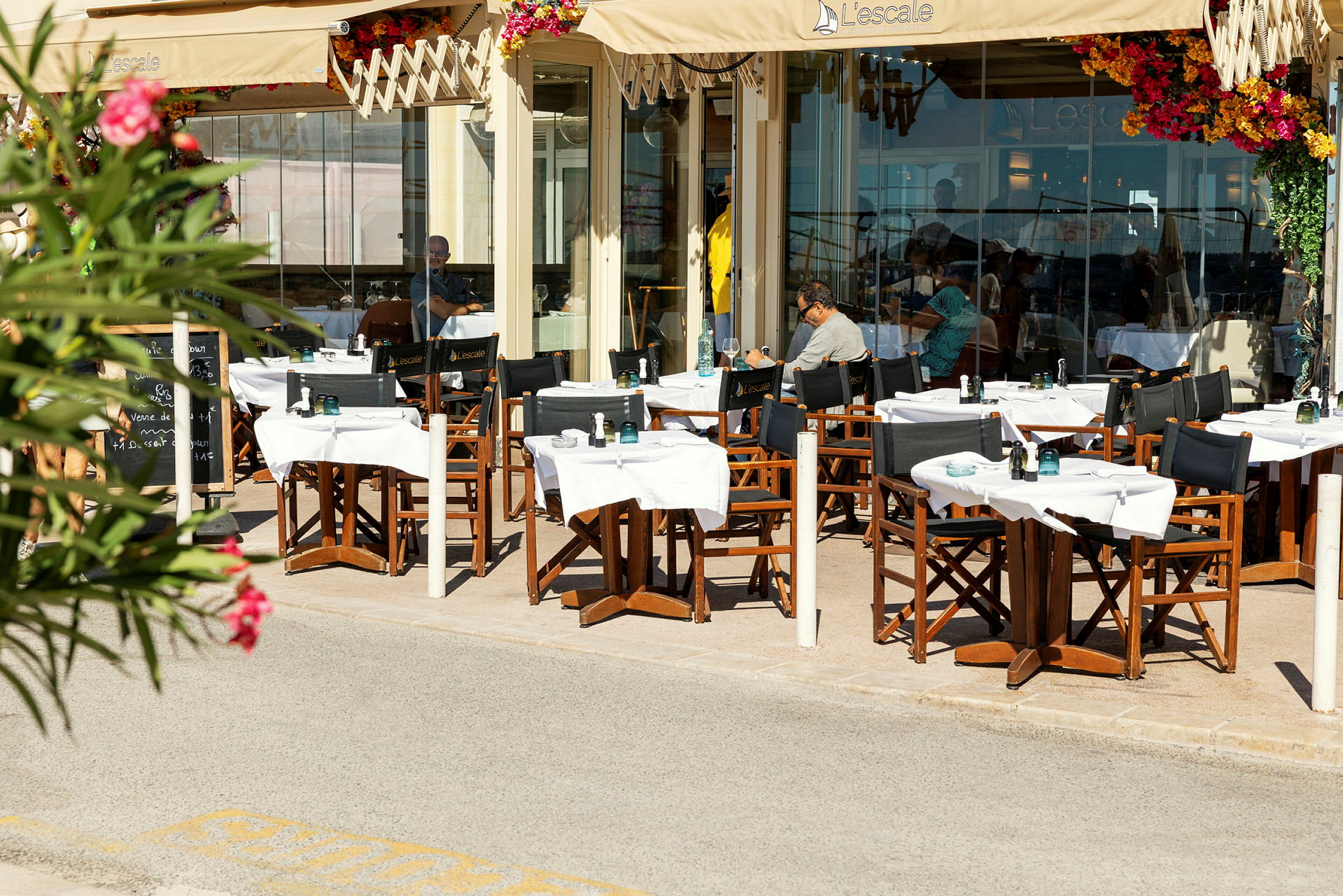 Udendørs serveringsområde ved en restaurant med borde og stole under en markise. (AI-genereret tekst)