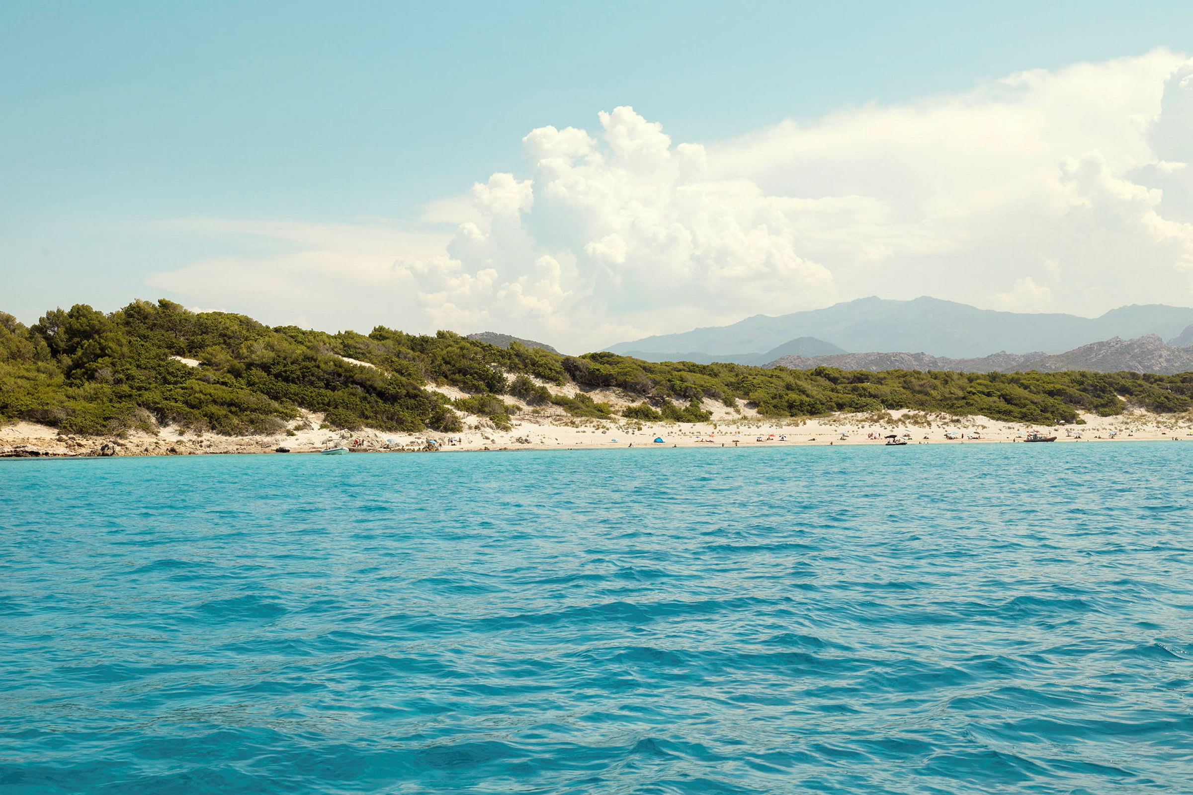 En strand med turkis vand, omgivet af grøn vegetation og bjerge i baggrunden. (AI-genereret tekst)
