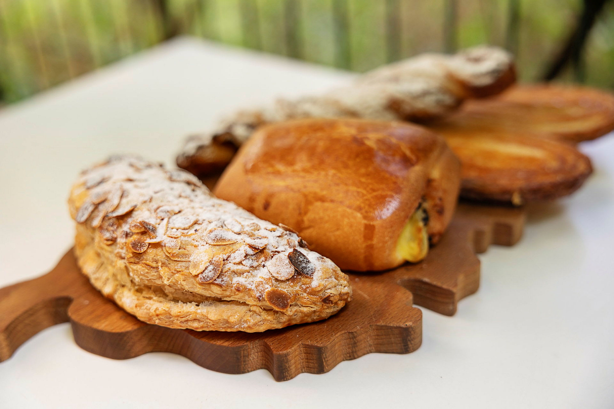 En træbakke med forskellige bagværk, herunder en mandelcroissant med flormelis. (AI-genereret tekst)