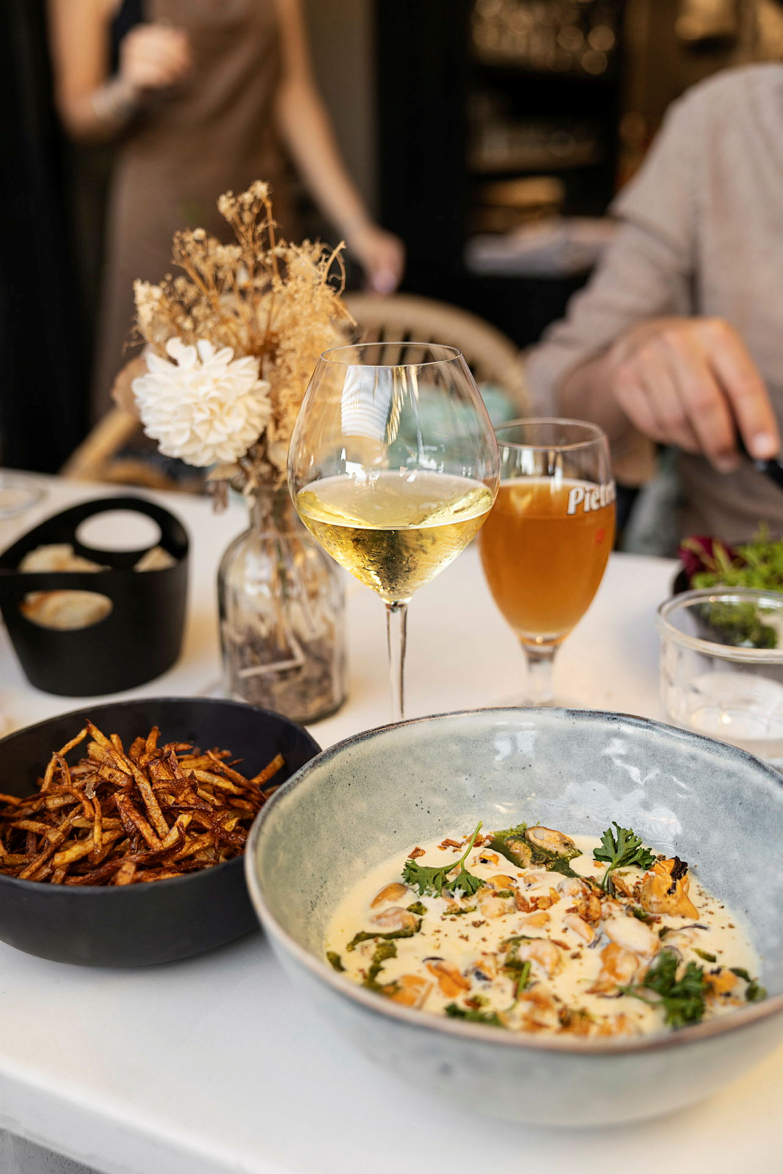 En tallerken med mad, et glas hvidvin og en skål med pommes frites på et bord. (AI-genereret tekst)