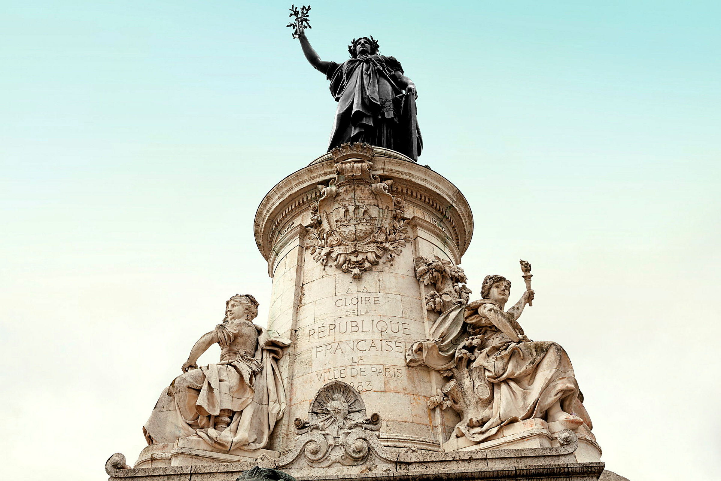 Statue med detaljeret kunstværk og inskriptioner på en stenbase med klar himmel i baggrunden. (AI-genereret tekst)