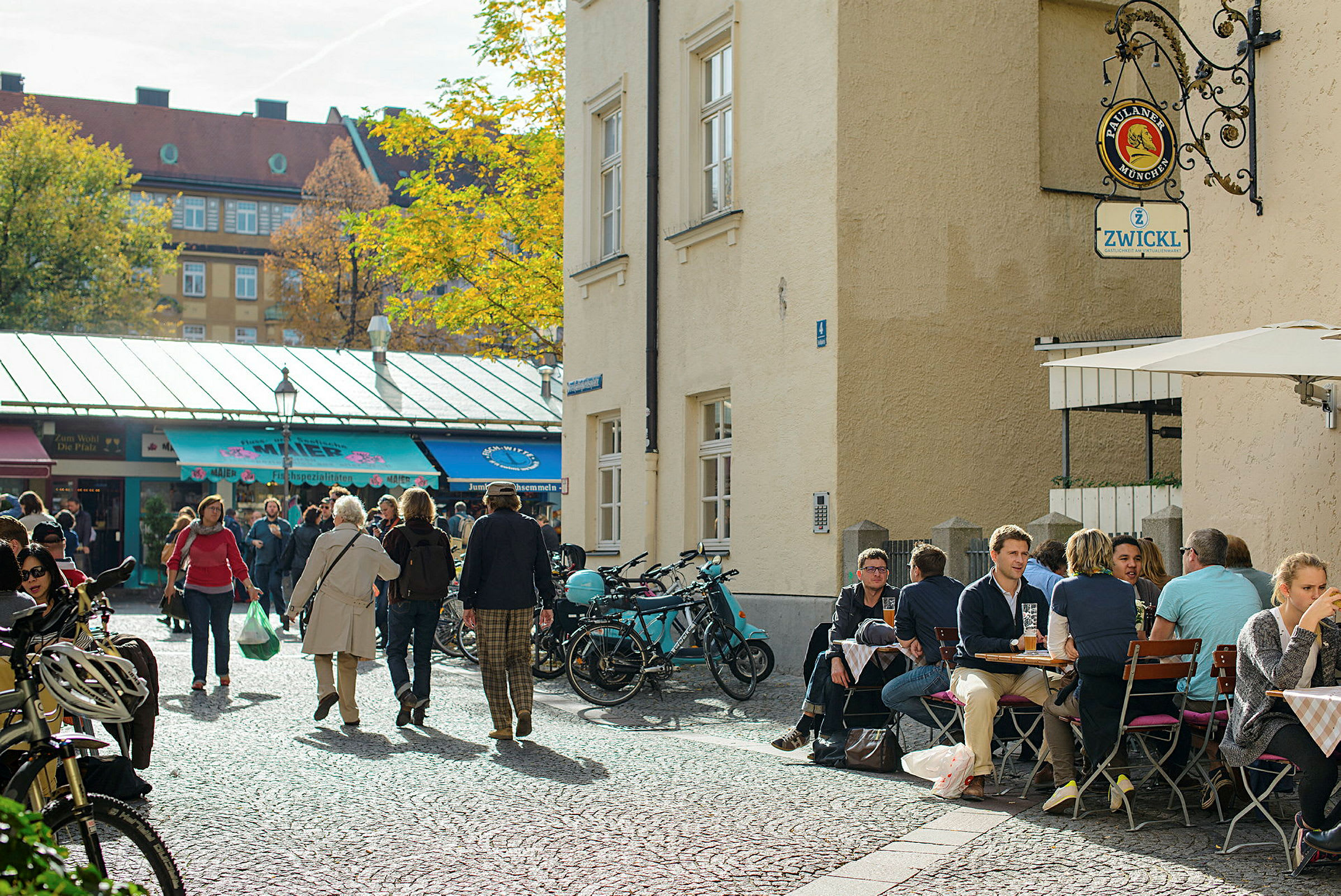 Et torv med mennesker, cykler og en café med udendørs servering. (AI-genereret tekst)