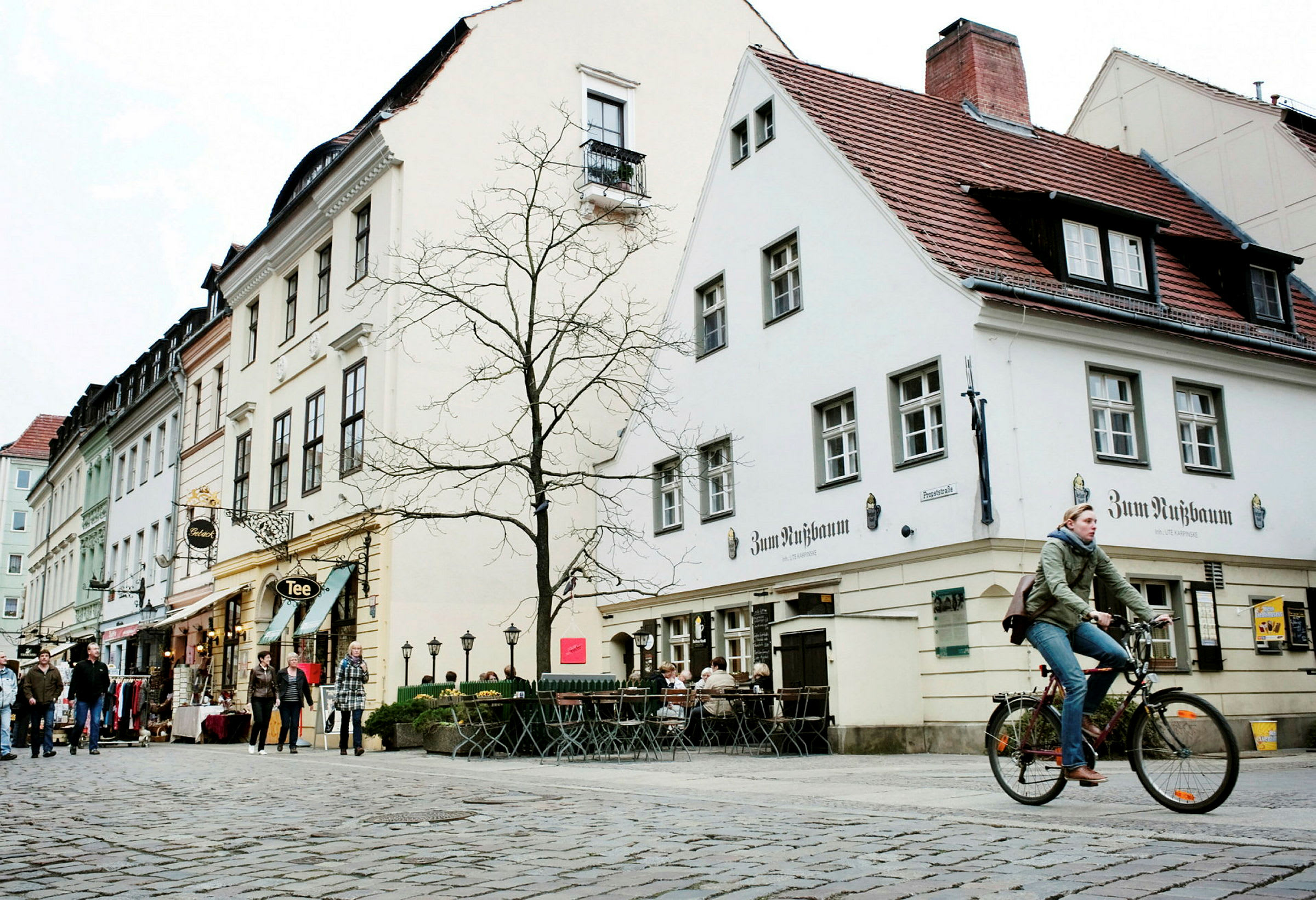 En brolagt gade omgivet af bygninger, en person gående og en person på cykel. (AI-genereret tekst)