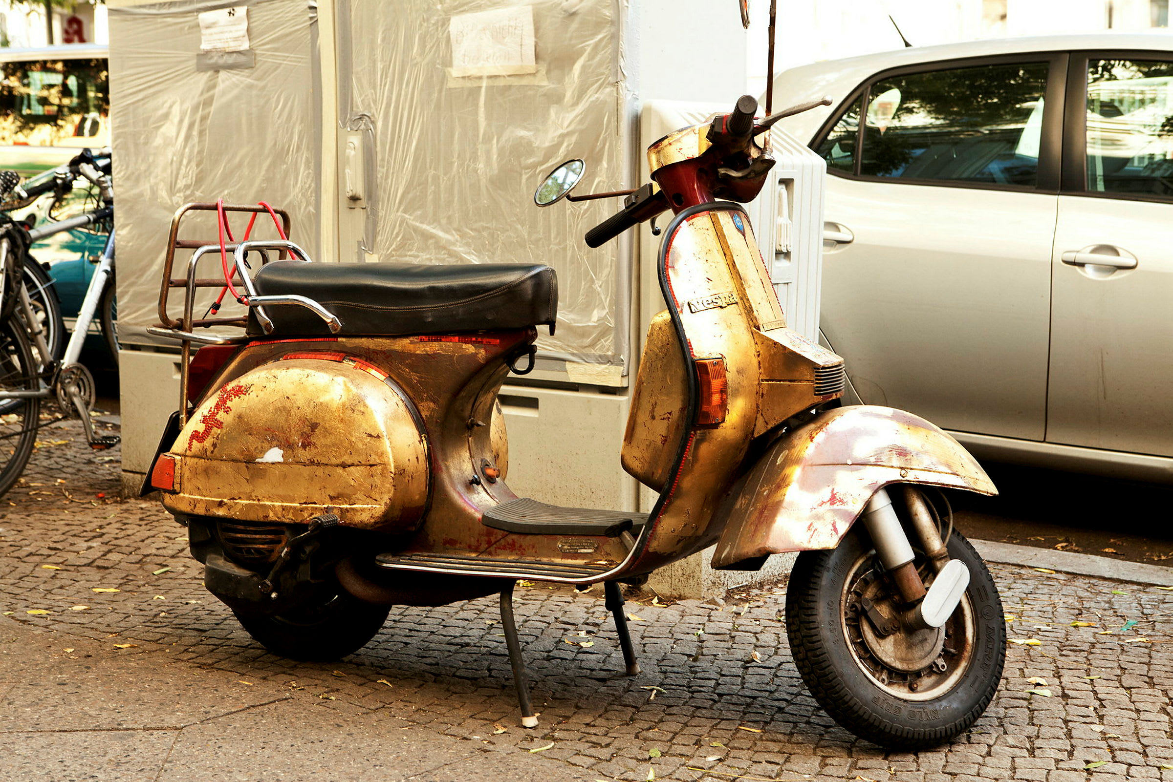 En gammel guldfarvet scooter står parkeret på et fortov ved siden af andre køretøjer. (AI-genereret tekst)