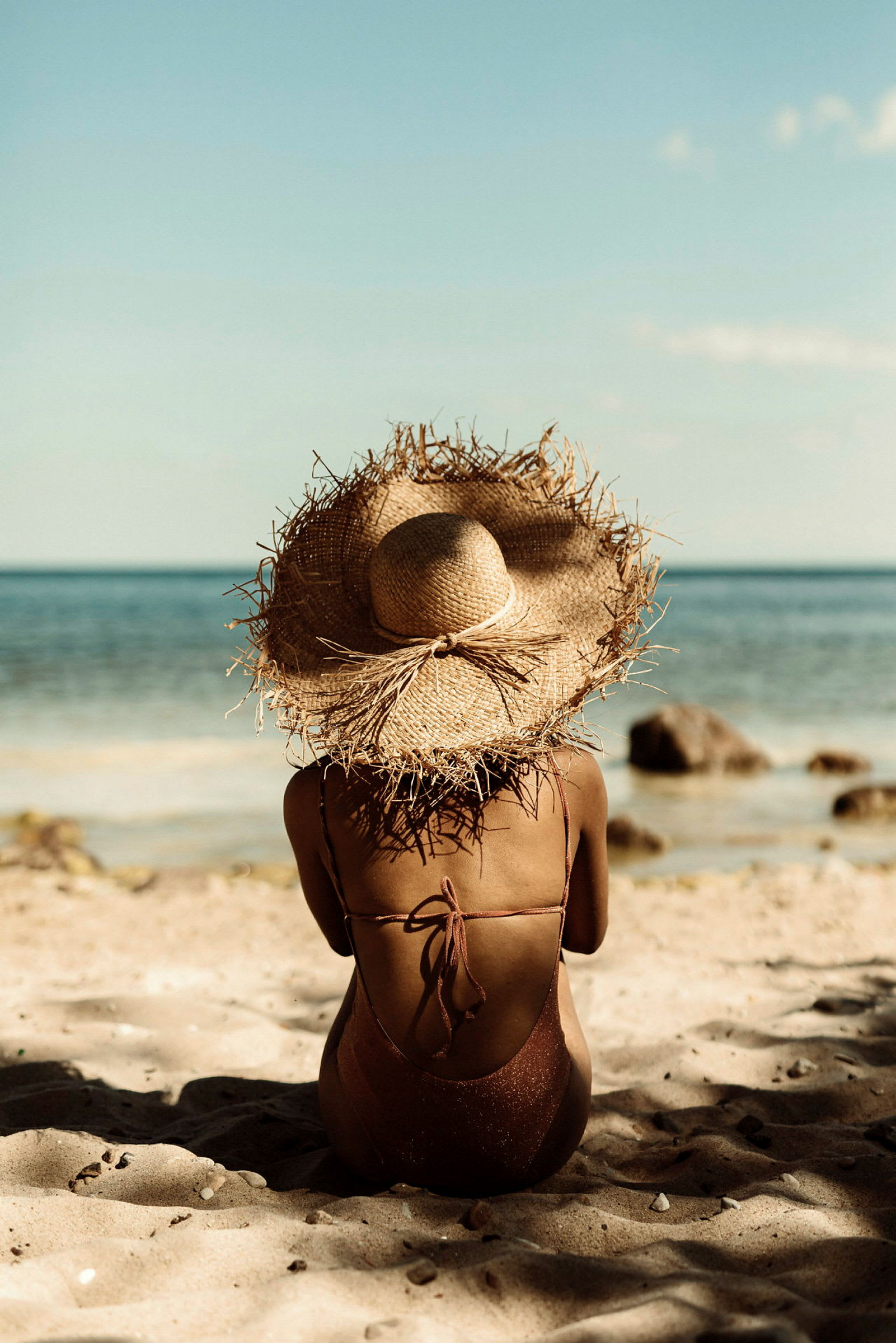 En person med solhat sidder på stranden med havet i baggrunden. (AI-genereret tekst)
