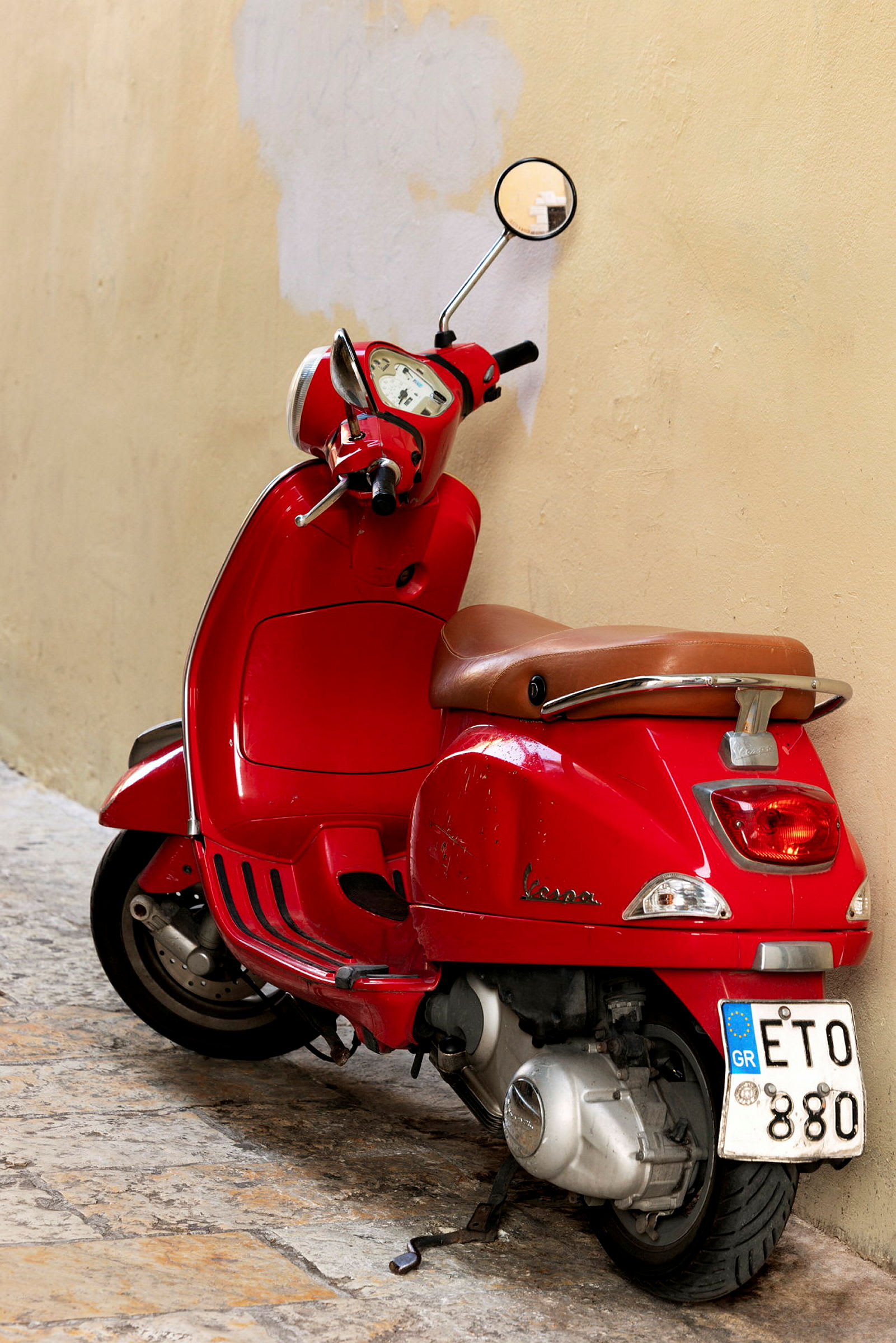 En rød scooter læner sig op ad en beige væg. (AI-genereret tekst)