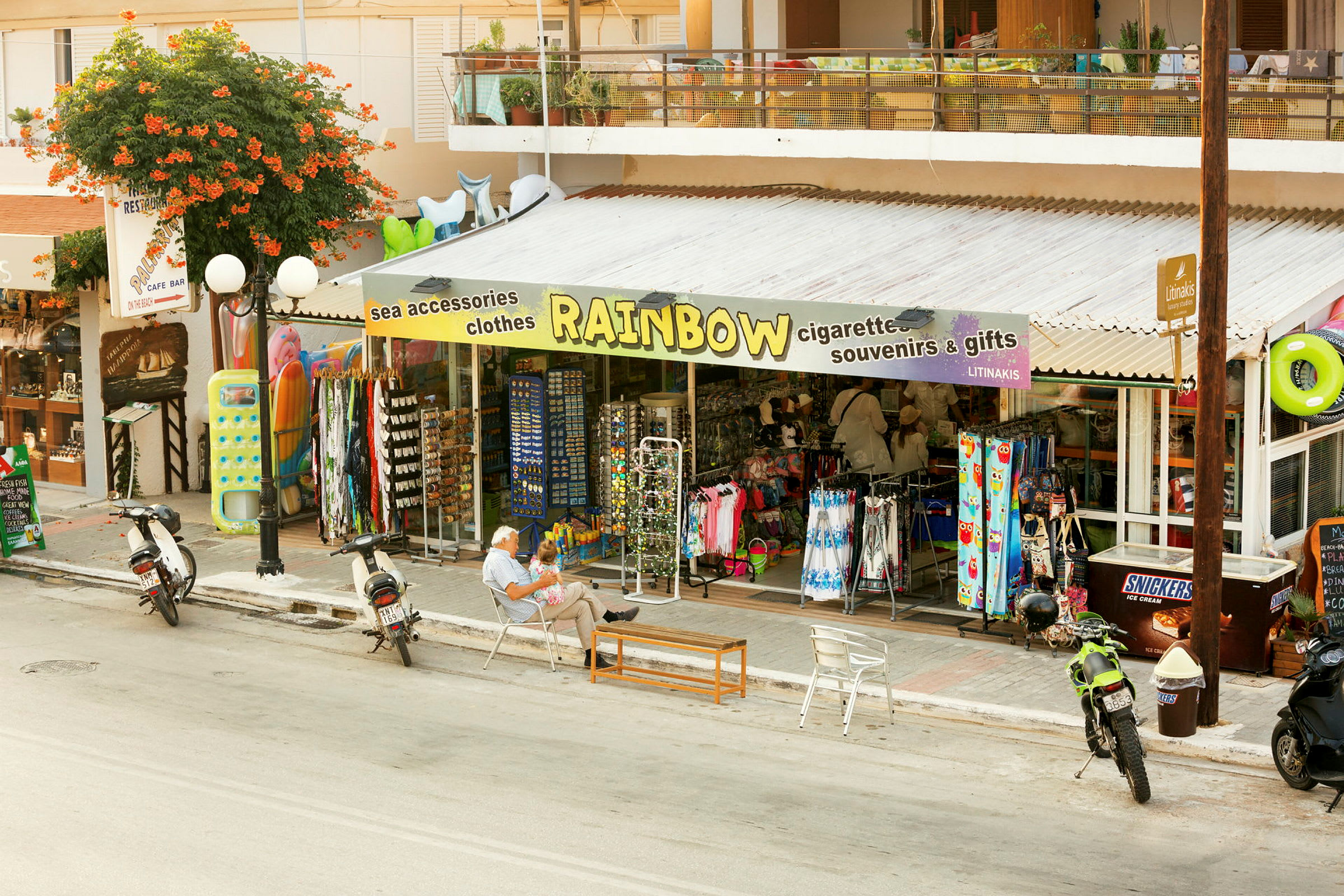 En butik med teksten 'Rainbow' på markisen sælger souvenirs og strandtilbehør. (AI-genereret tekst)