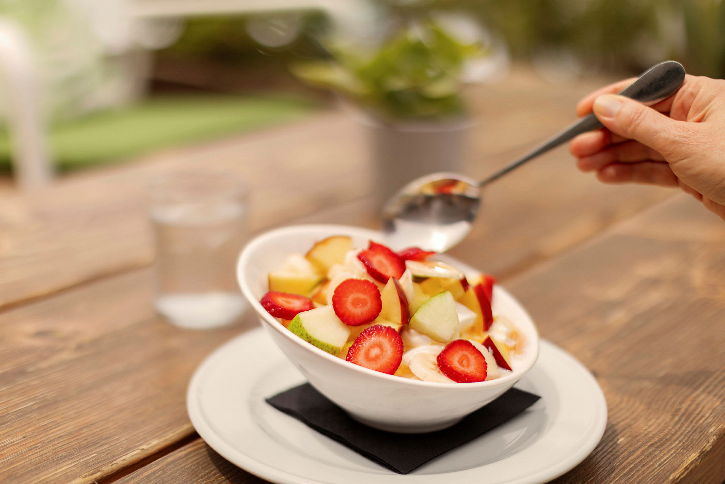 En skål med frugtsalat med jordbær, æblestykker og bananskiver, serveret på et bord. (AI-genereret tekst)