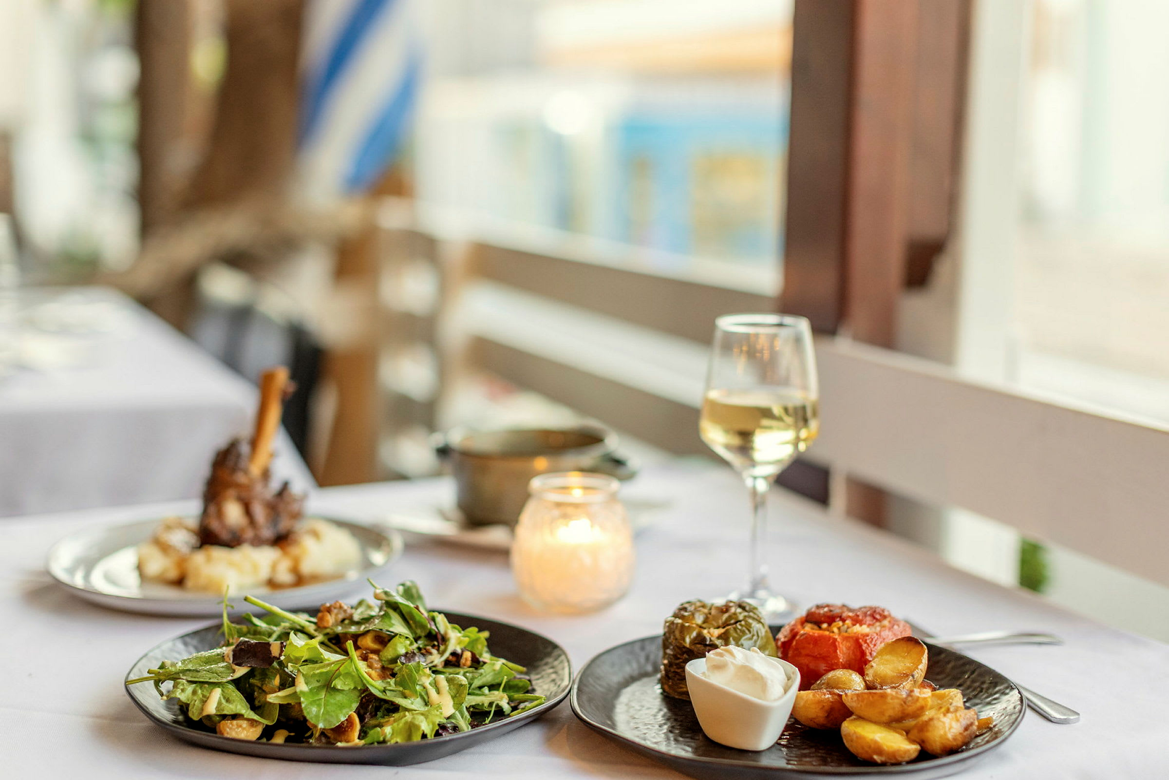 En bordscene med mad serveret, herunder salat, fyldte grøntsager og kartofler, samt et glas hvidvin. (AI-genereret tekst)