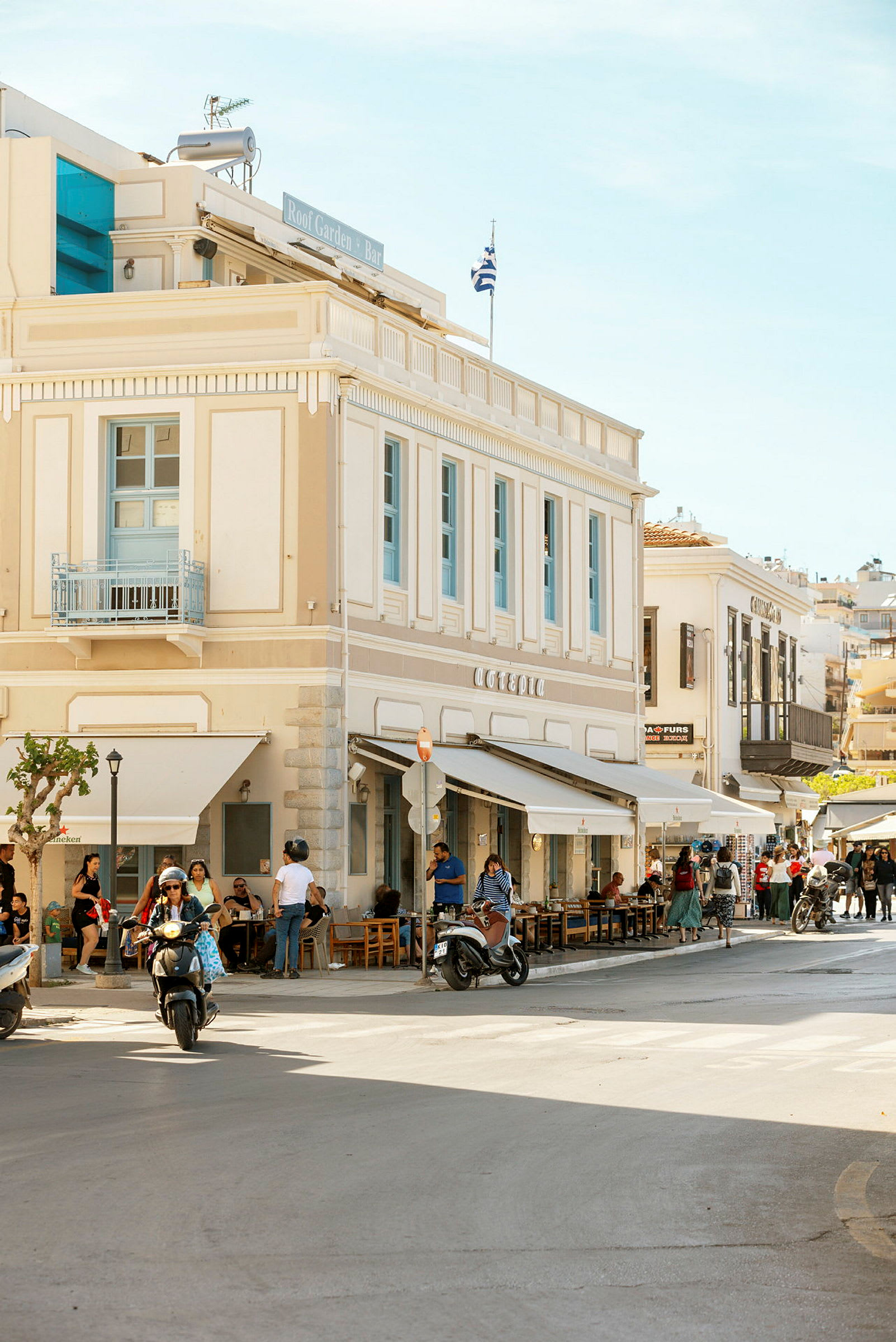 En gade, der går forbi en bygning med café, hvor folk sidder ved borde og motorcykler kører forbi. (AI-genereret tekst)