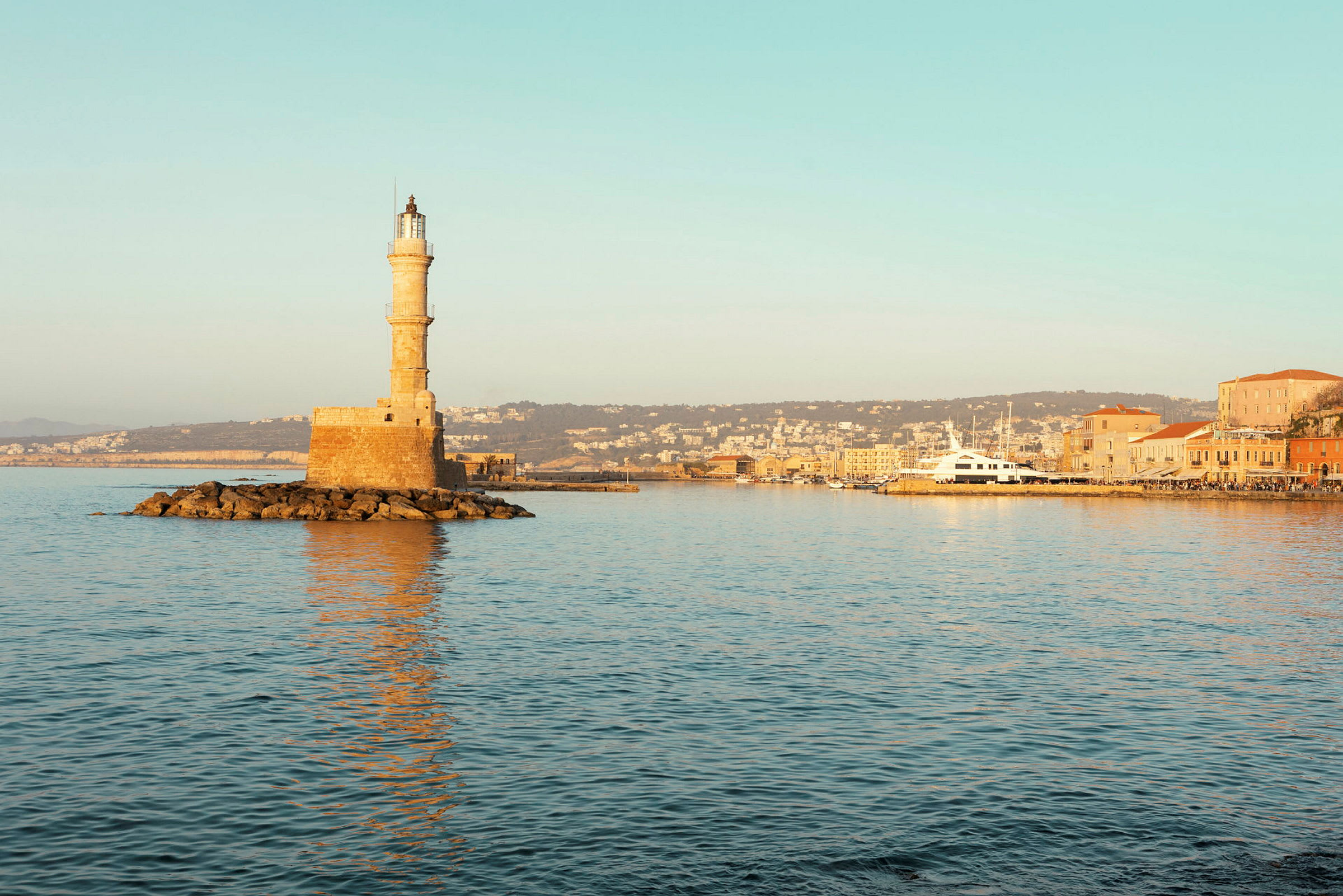 Billede af et fyrtårn på en stenede placering ved havet med bykysten i baggrunden. (AI-genereret tekst)