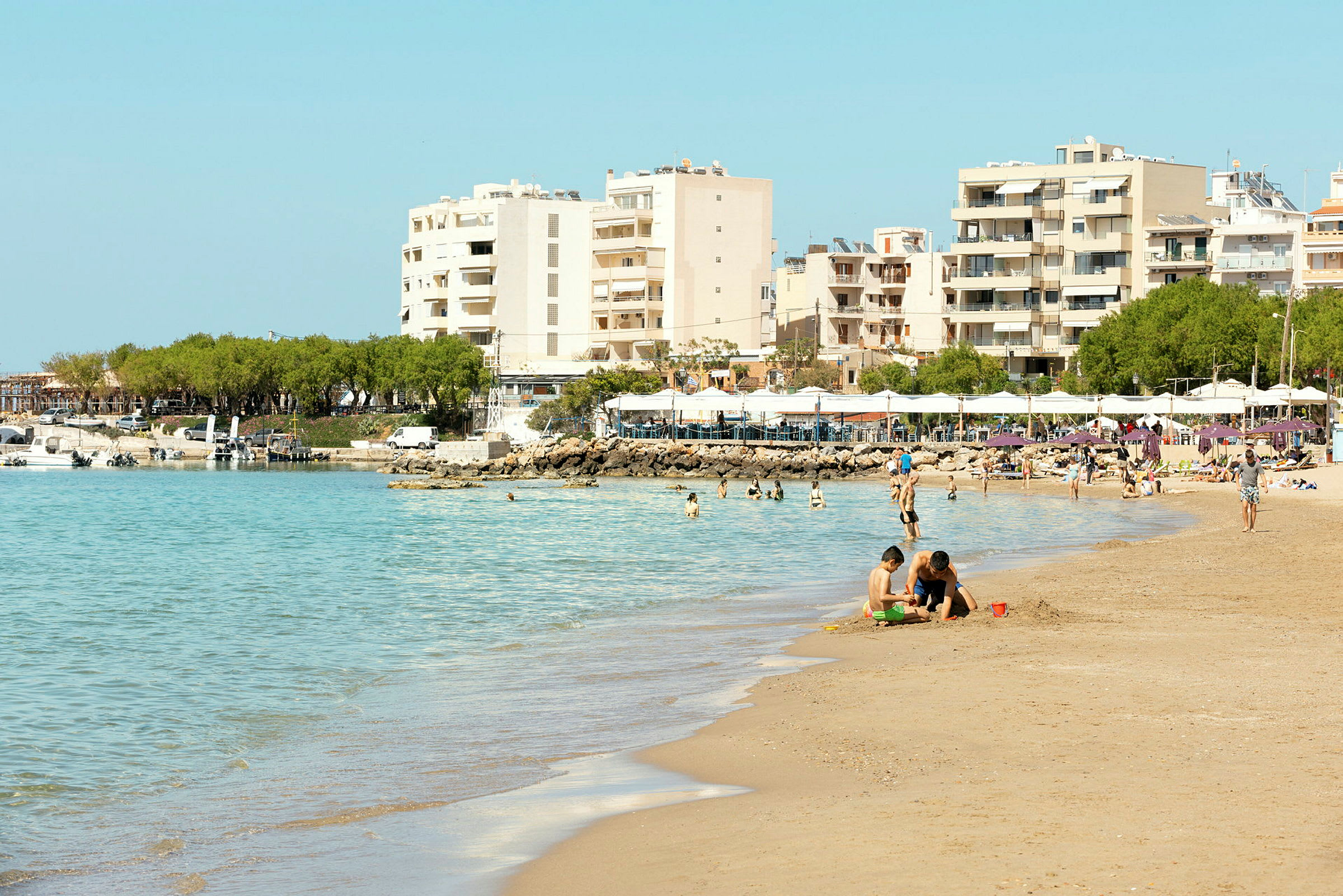 Billede af en strand med badende personer, bygninger i baggrunden. (AI-genereret tekst)