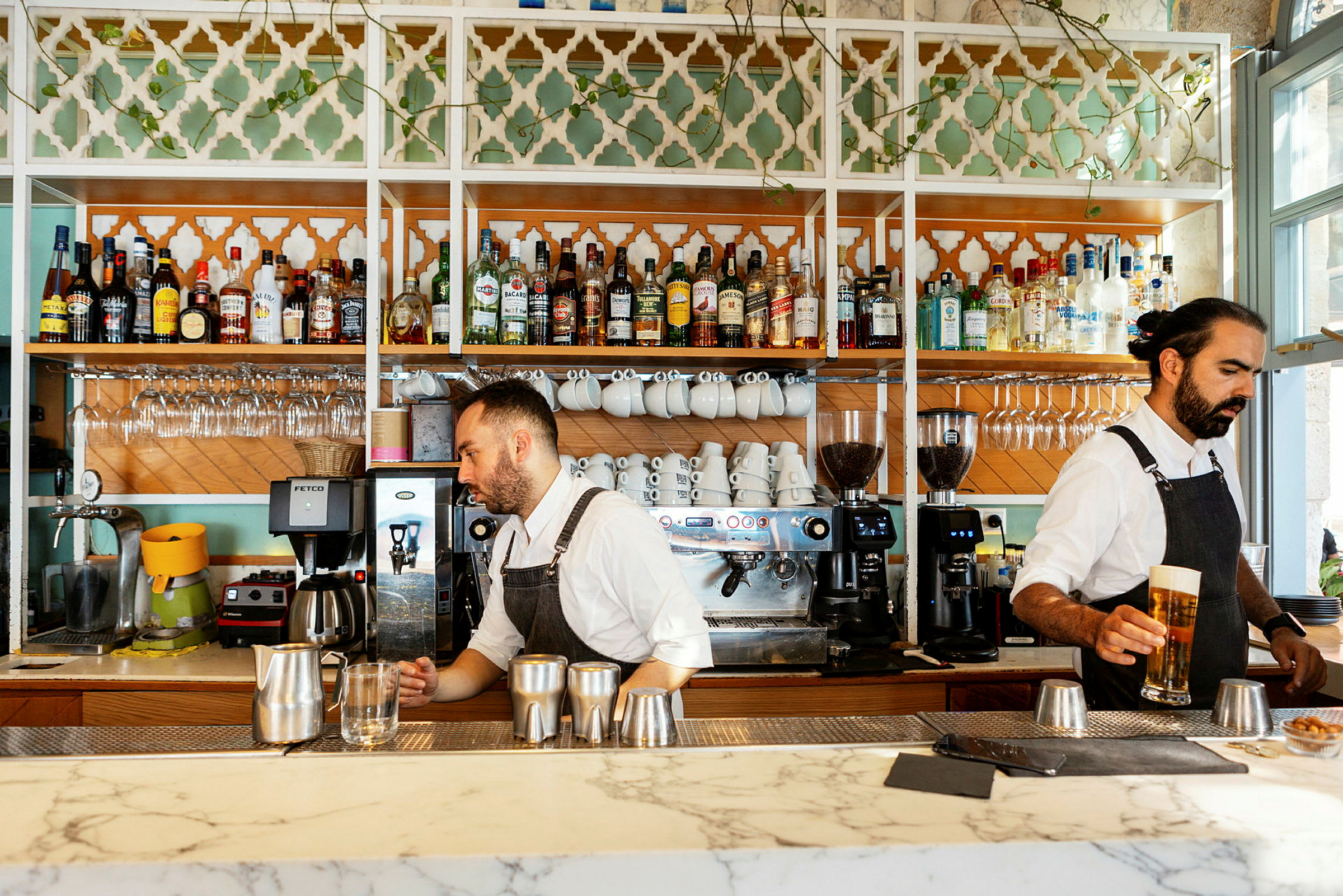 En bar med vitrineskabe fyldt med spiritusflasker, kaffekopper og glas. Kaffemaskiner står på bardisken. (AI-genereret tekst)