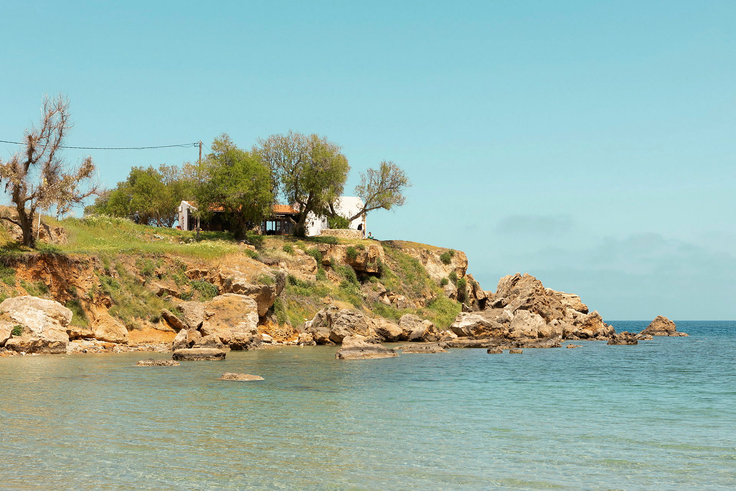 Et hus på en klippe ved havet med klart blåt vand. (AI-genereret tekst)