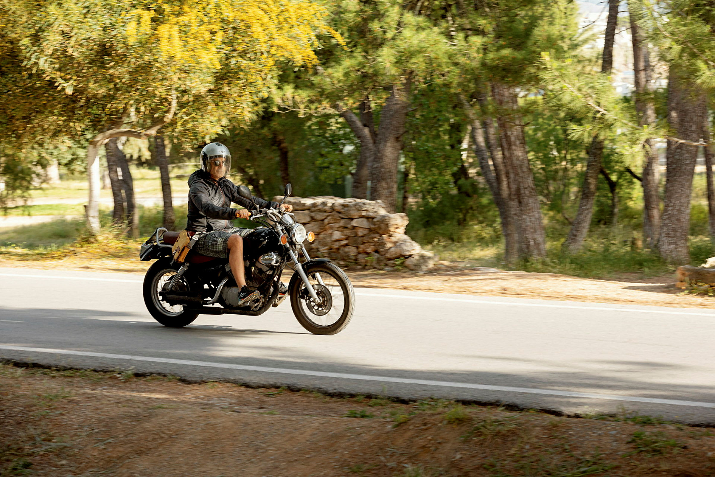 En person kører på en motorcykel på en vej omgivet af grøntområder. (AI-genereret tekst)