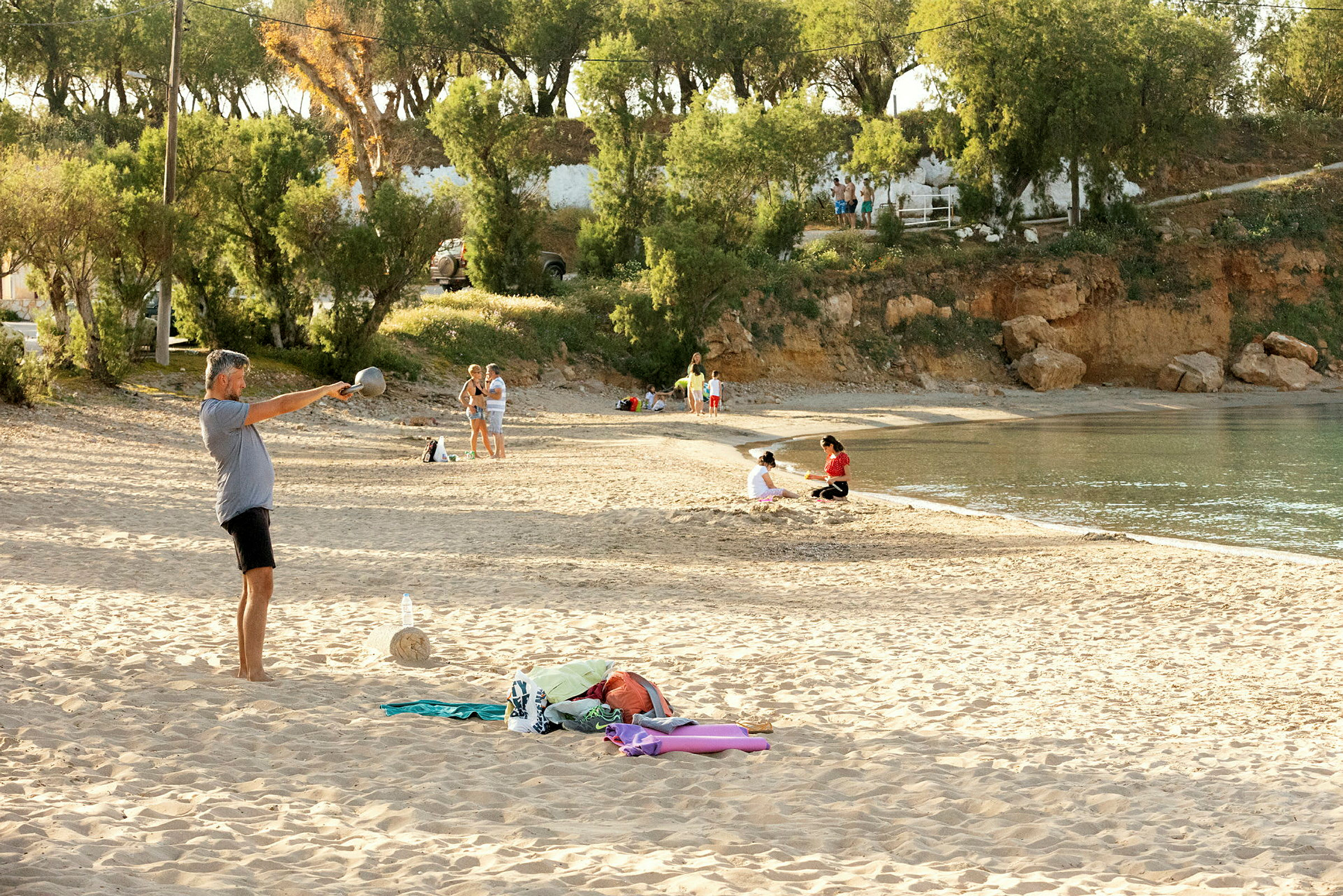Strand med mennesker på sanden og ved vandkanten, omgivet af træer og klipper. (AI-genereret tekst)