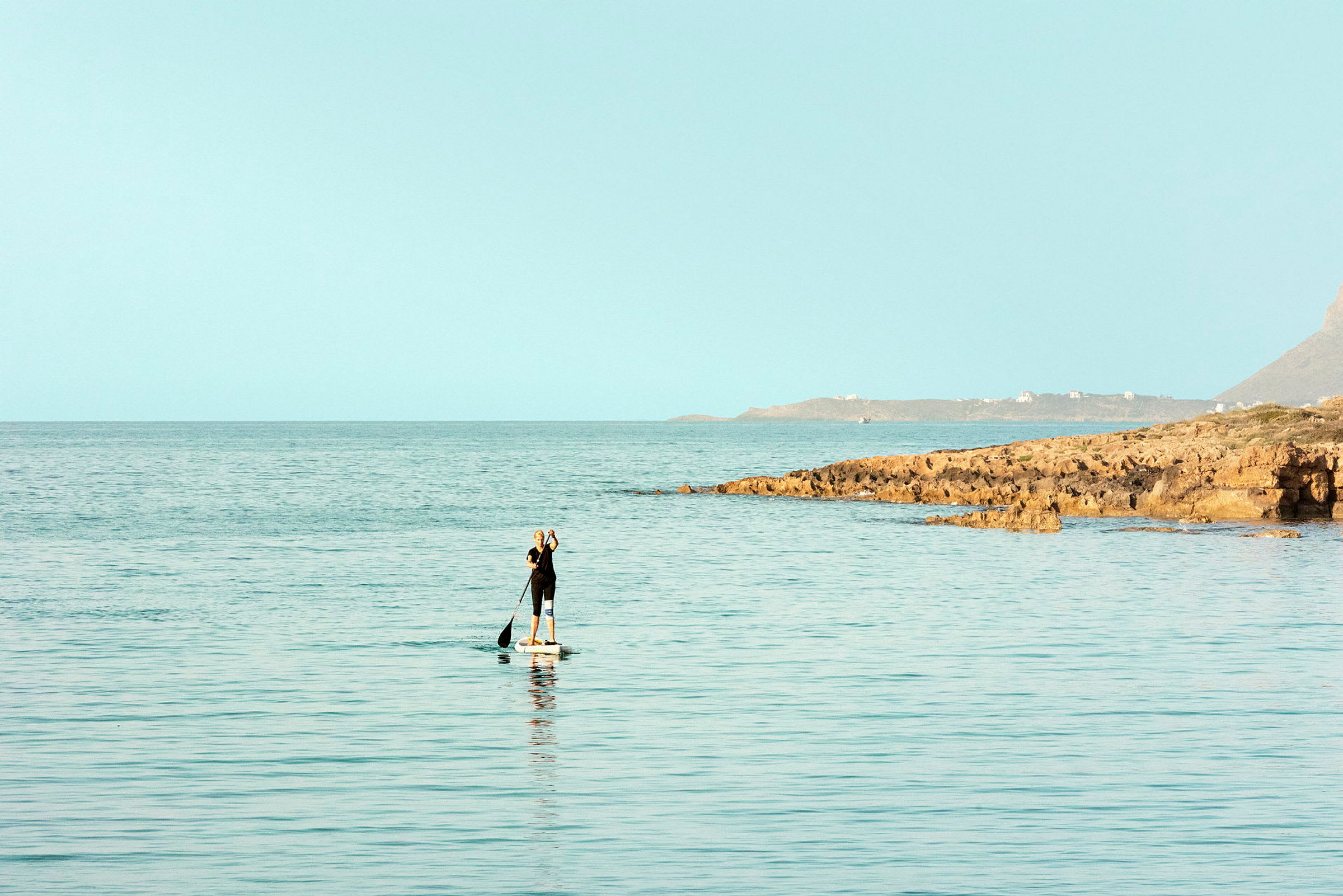 En person, der padler på et paddleboard i havet tæt på en klippefyldt kyst. (AI-genereret tekst)