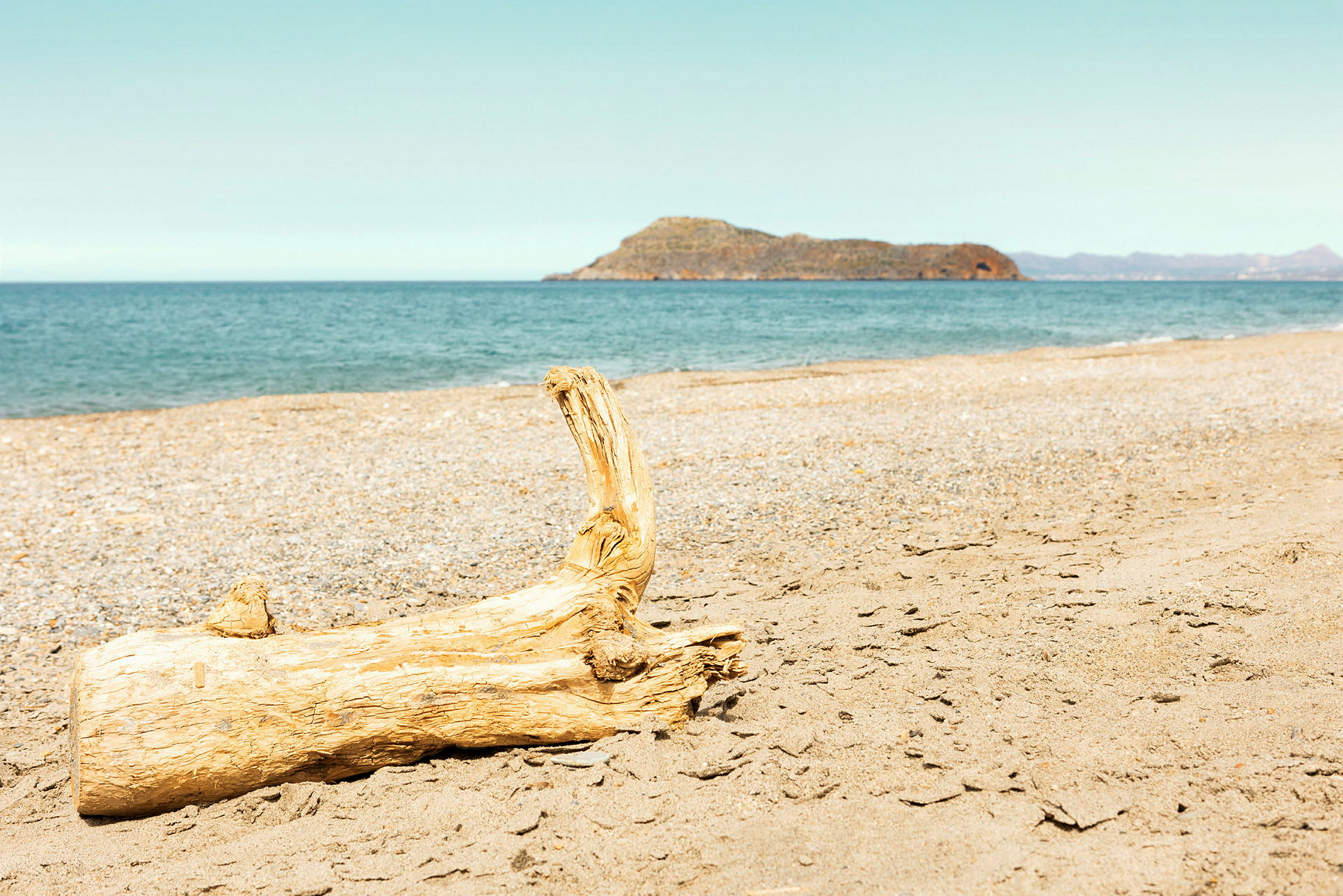 Et stykke træ ligger på stranden med havet og en bjergrig ø i baggrunden. (AI-genereret tekst)