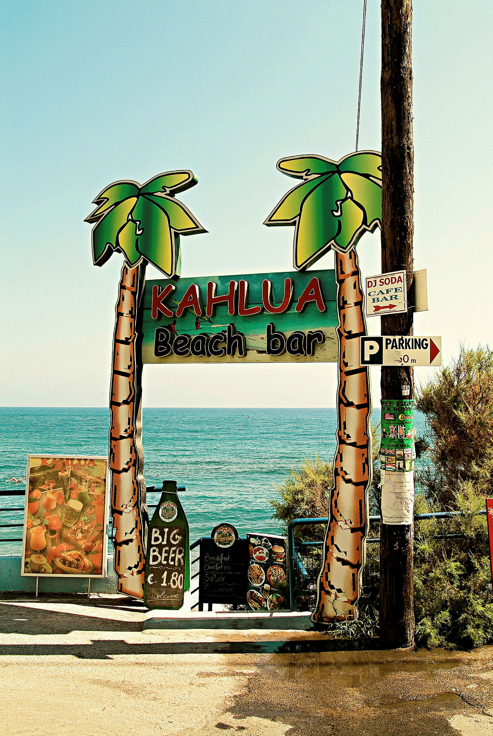Billede af et skilt med teksten 'Kahlua Beach Bar' foran havet. (AI-genereret tekst)