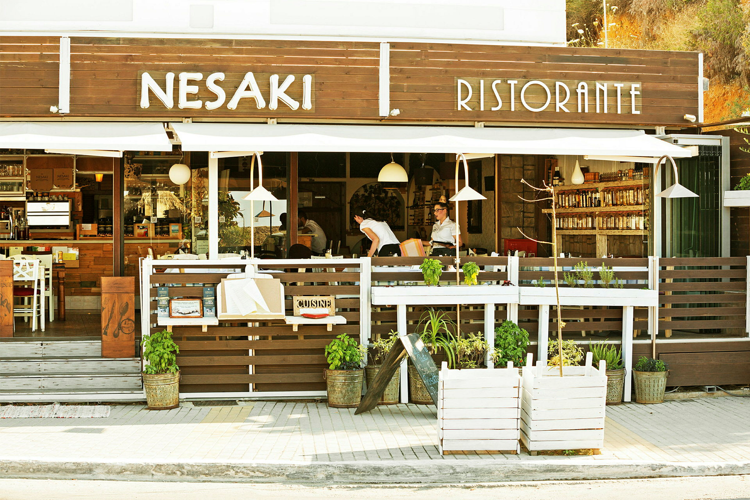 Billedet viser facaden af en restaurant med teksten "Nesaki Ristorante" over indgangen samt udendørs servering. (AI-genereret tekst)