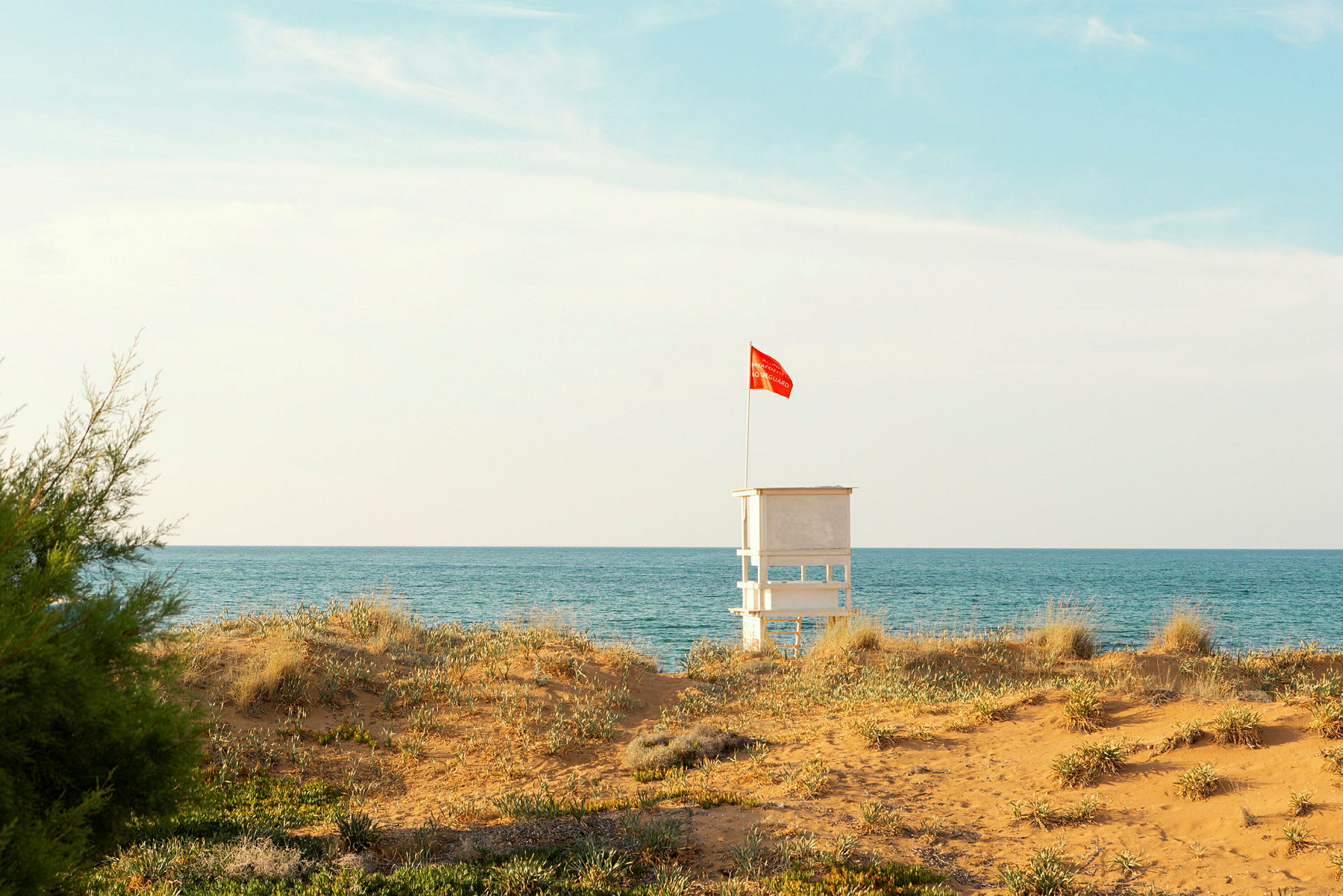 Strandudsigt med et livreddertårn og et rødt flag. (AI-genereret tekst)
