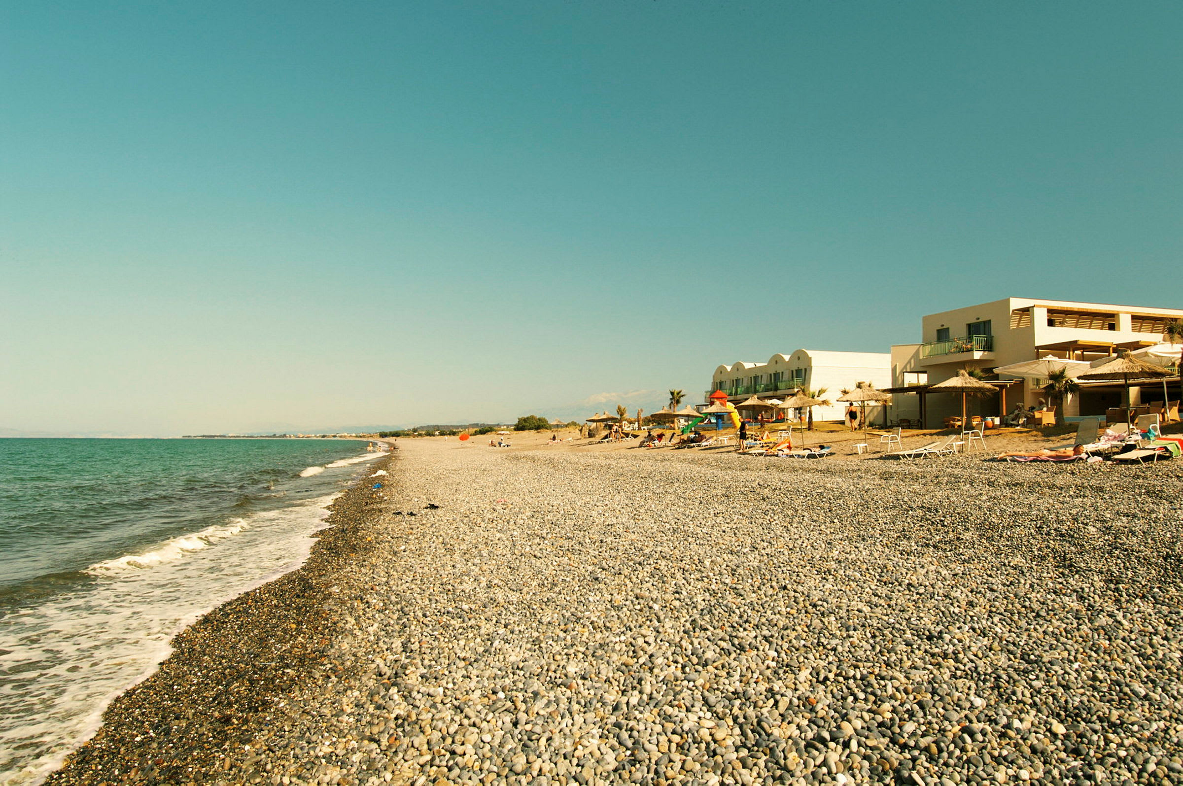 Strand med runde sten og hotelbygning i baggrunden. (AI-genereret tekst)