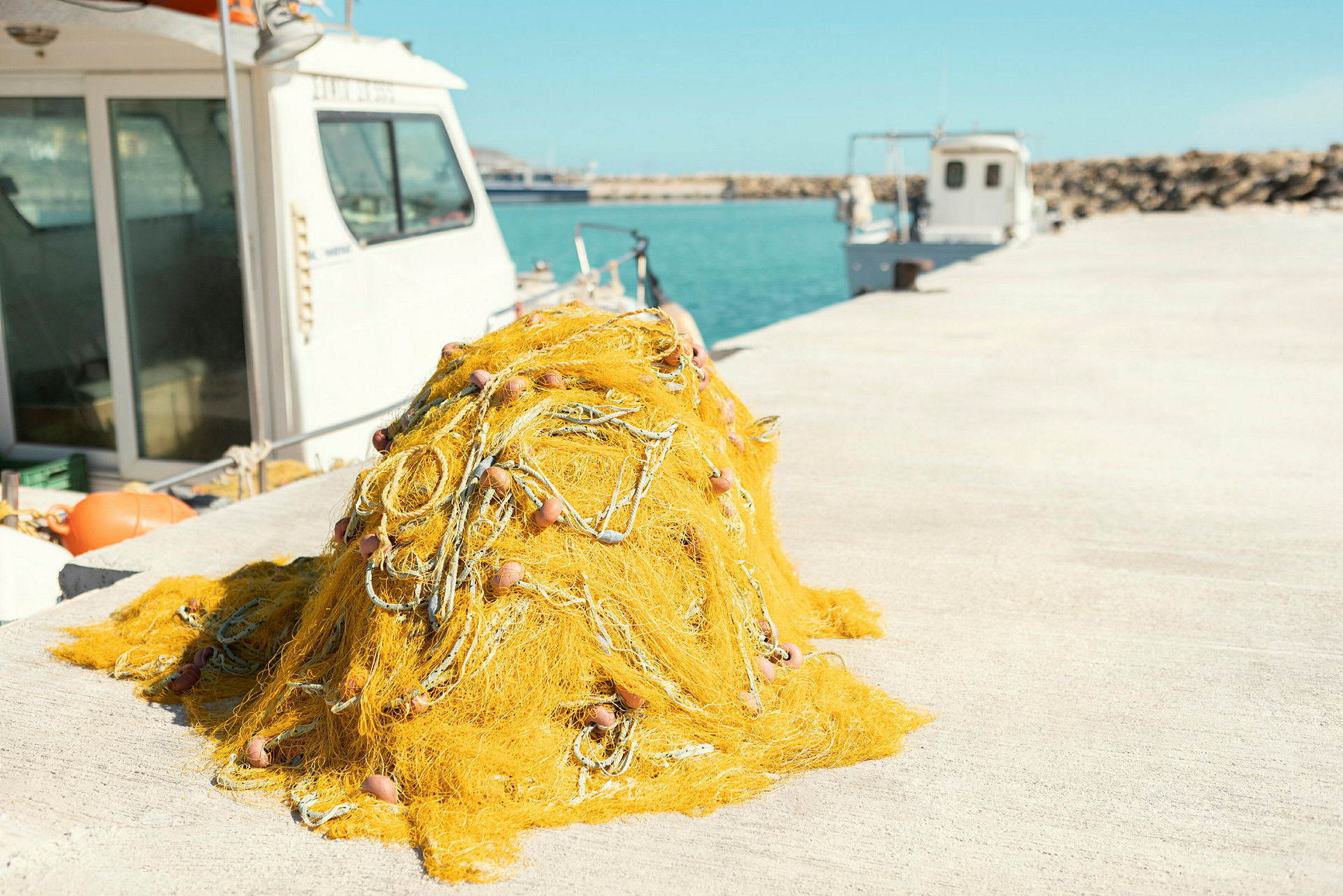 En bunke gult fiskenet ligger på en kaj, med både og havet i baggrunden. (AI-genereret tekst)