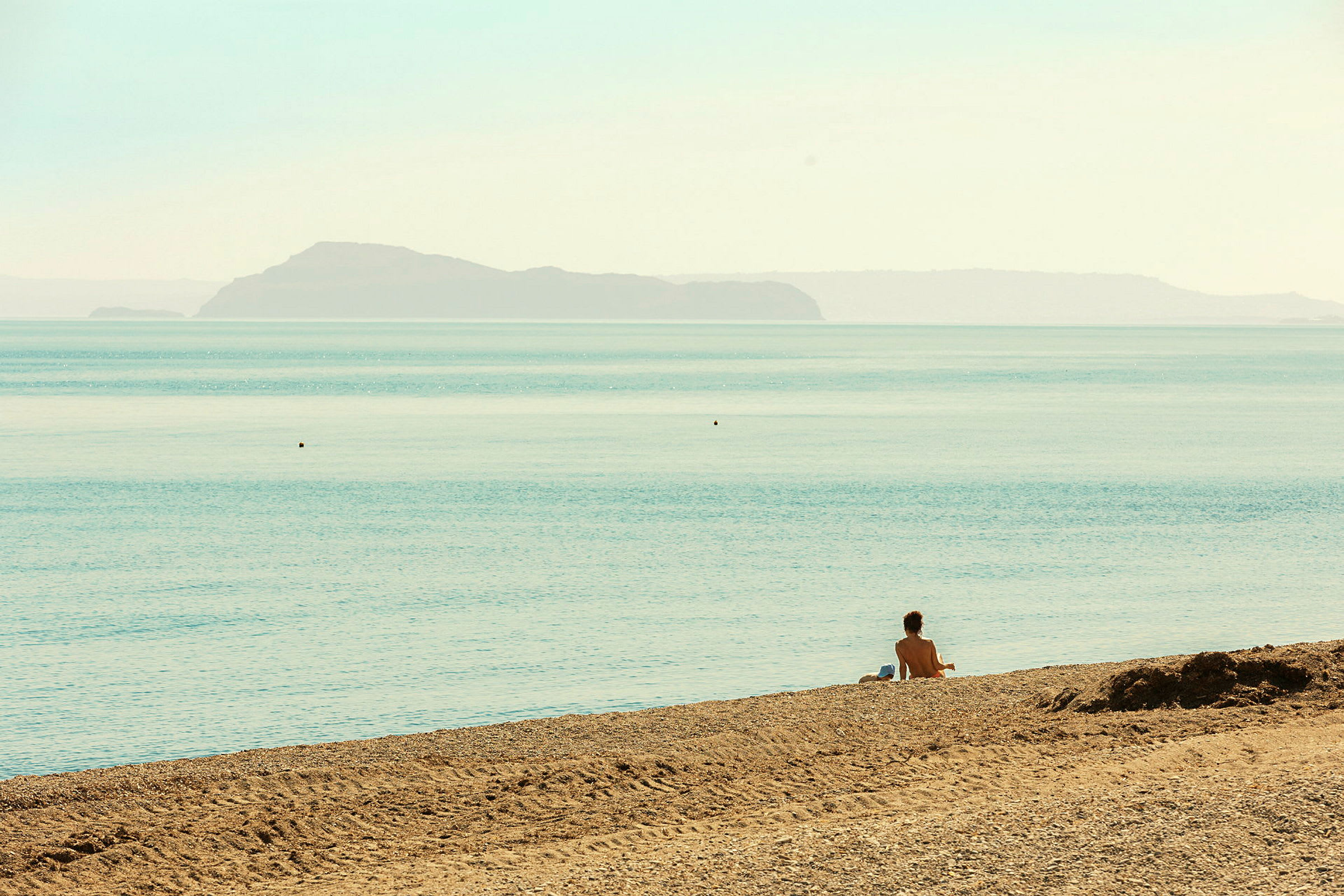 En person sidder på en sandstrand ved havet med en ø i baggrunden. (AI-genereret tekst)
