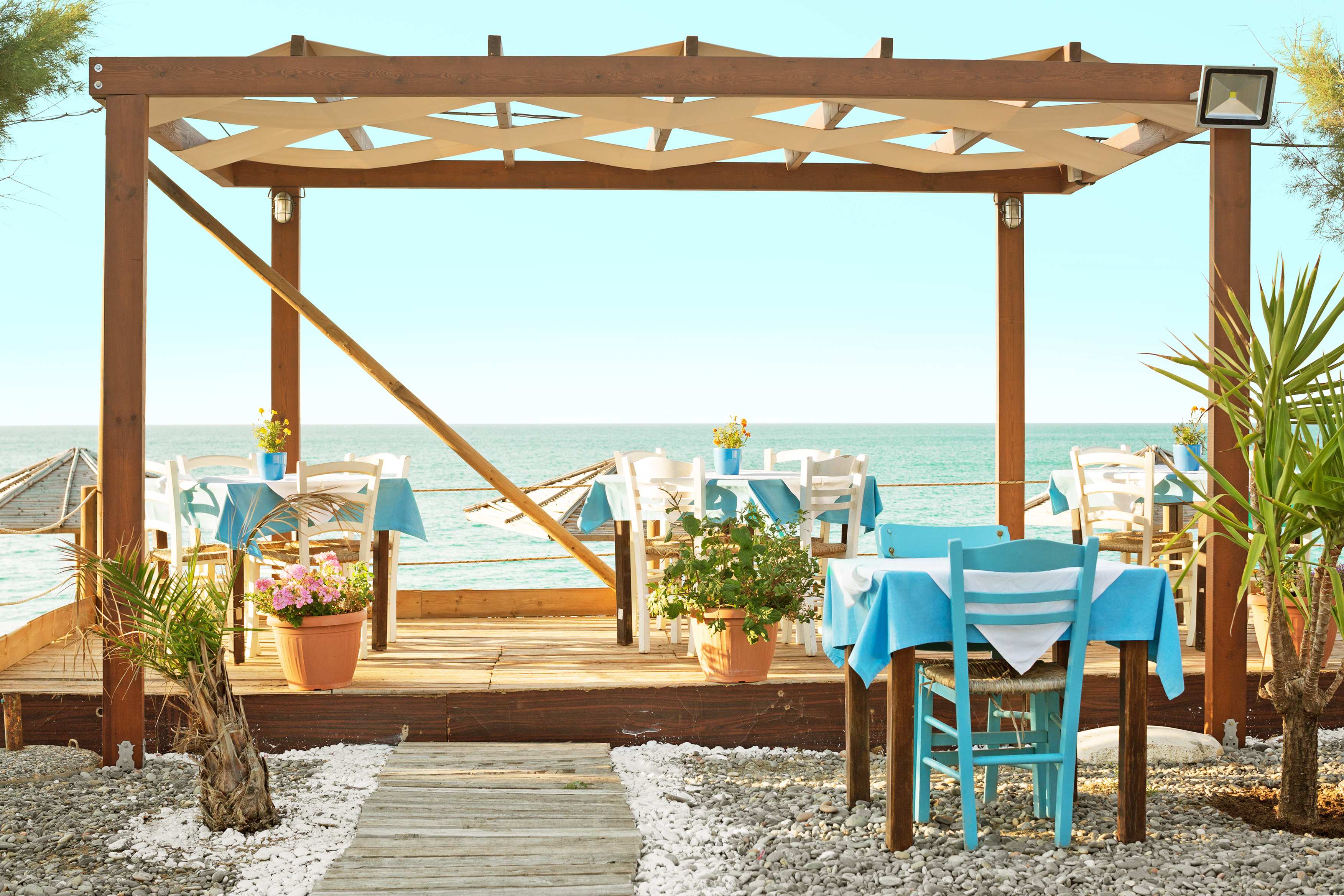 En restaurant nær havet med træpergola og blå duge på bordene. (AI-genereret tekst)